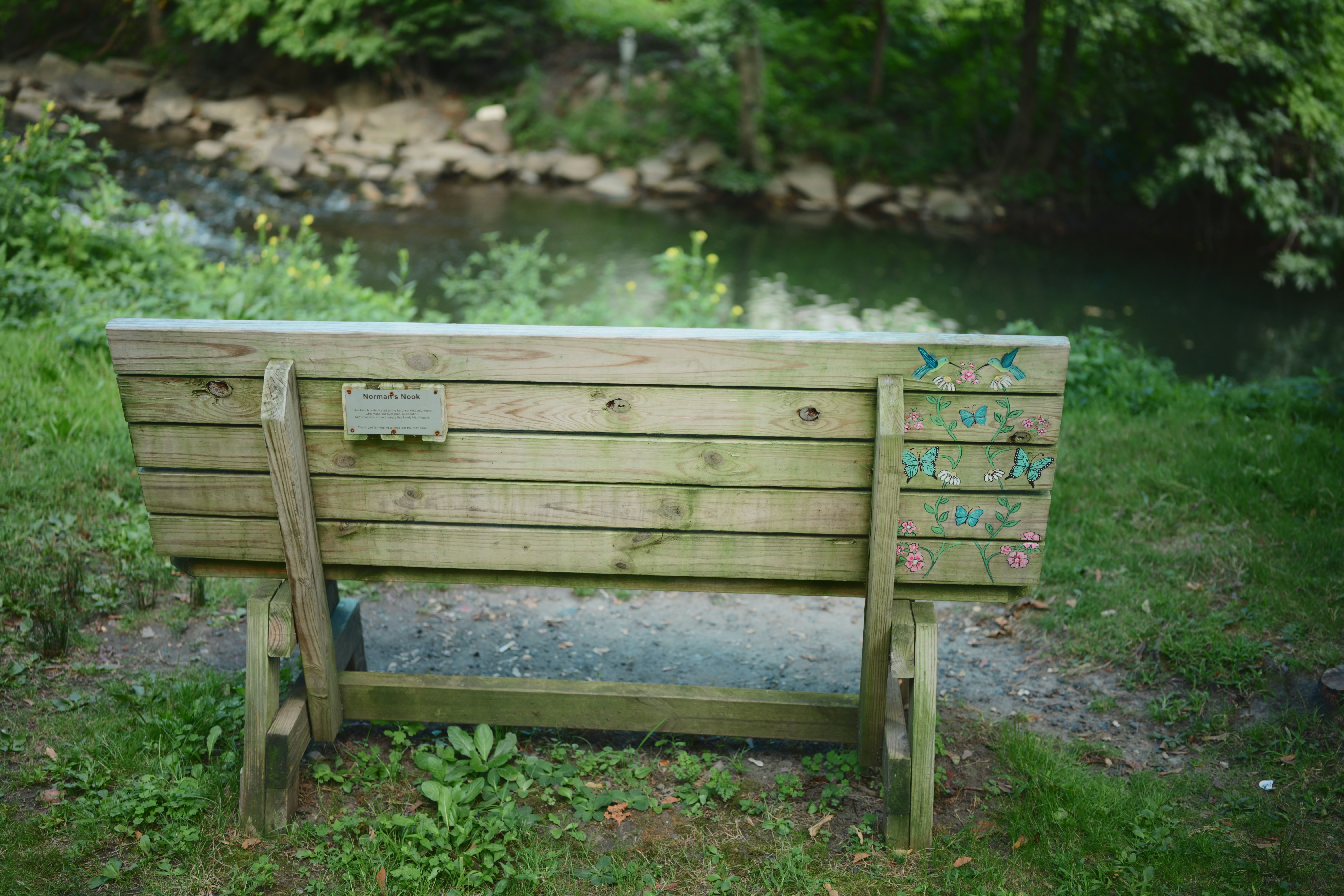 Weathered wooden bench with a stream and trees.