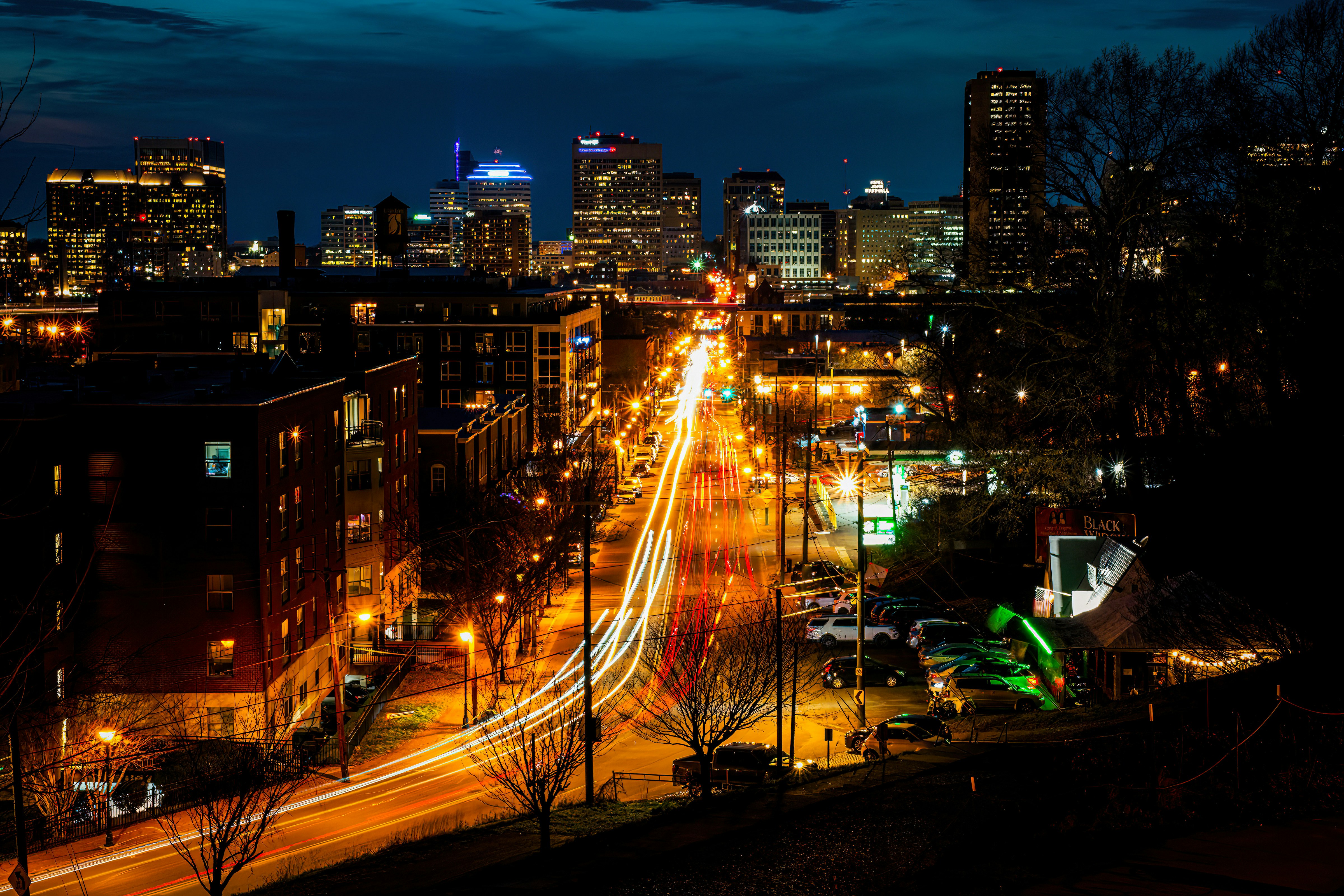 Vibrant city street and skyline at night with light trails.