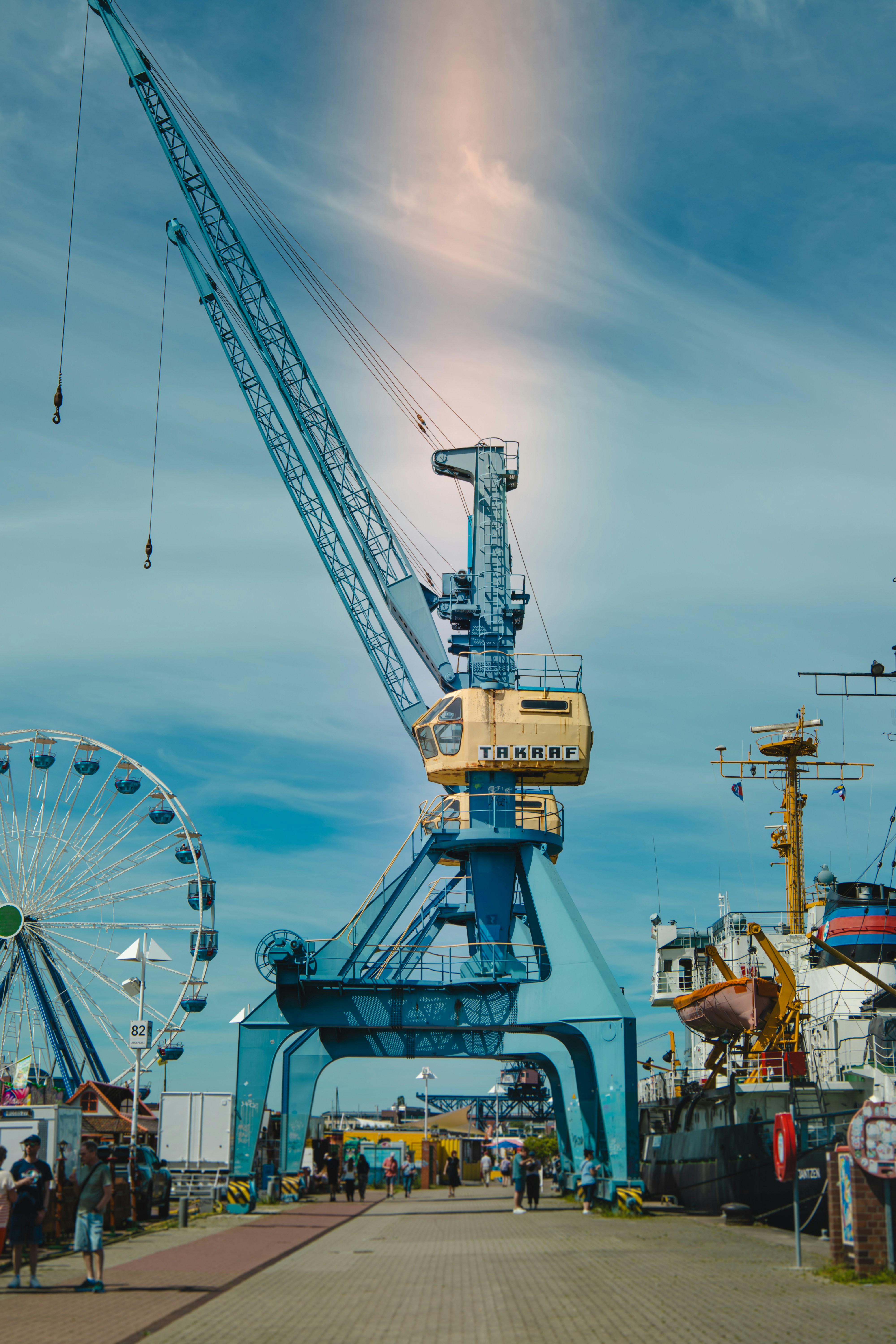 Industrial crane, ferris wheel, and ship at a vibrant port.