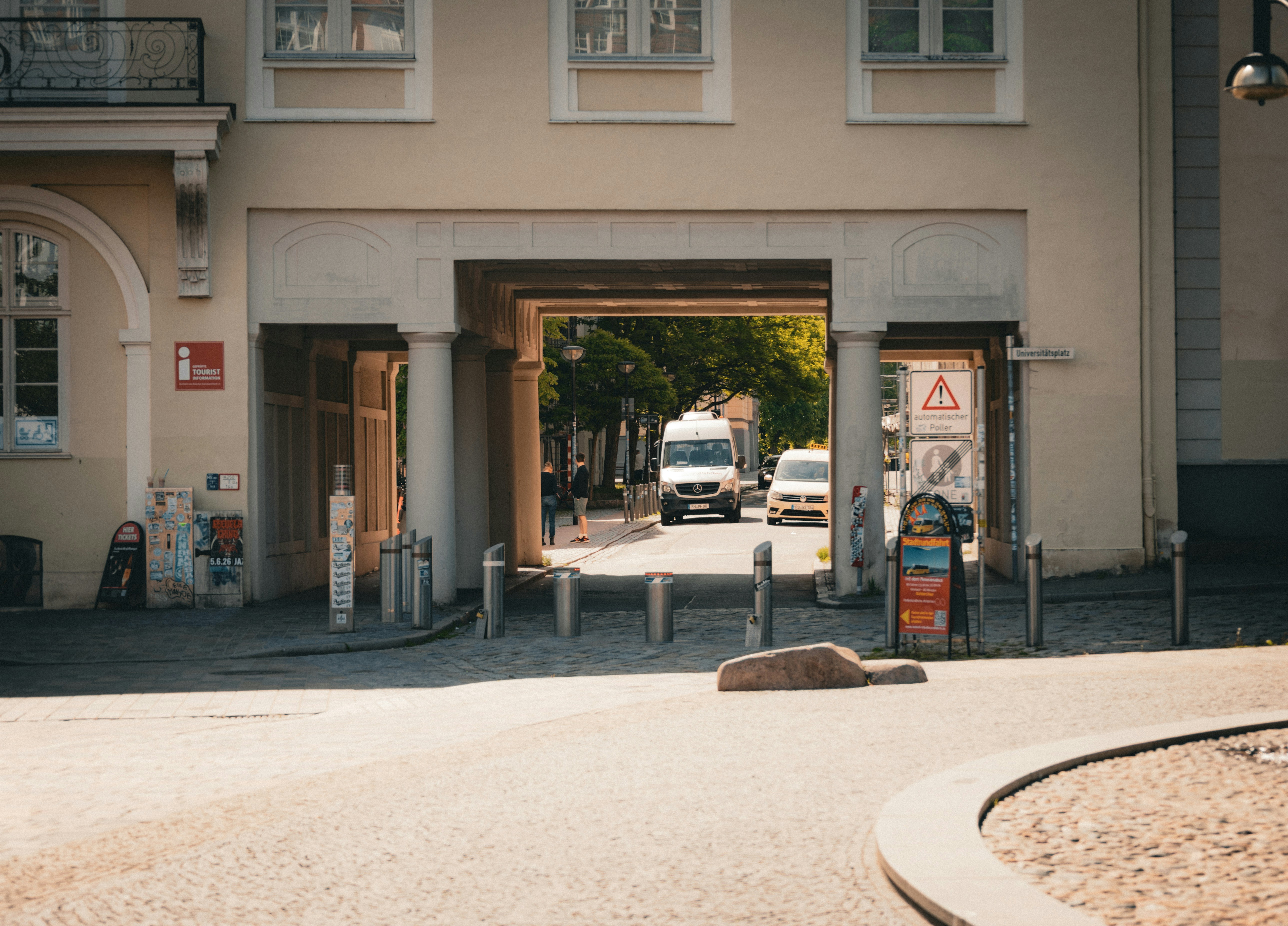 Cars driving through a building's archway on a sunny day.