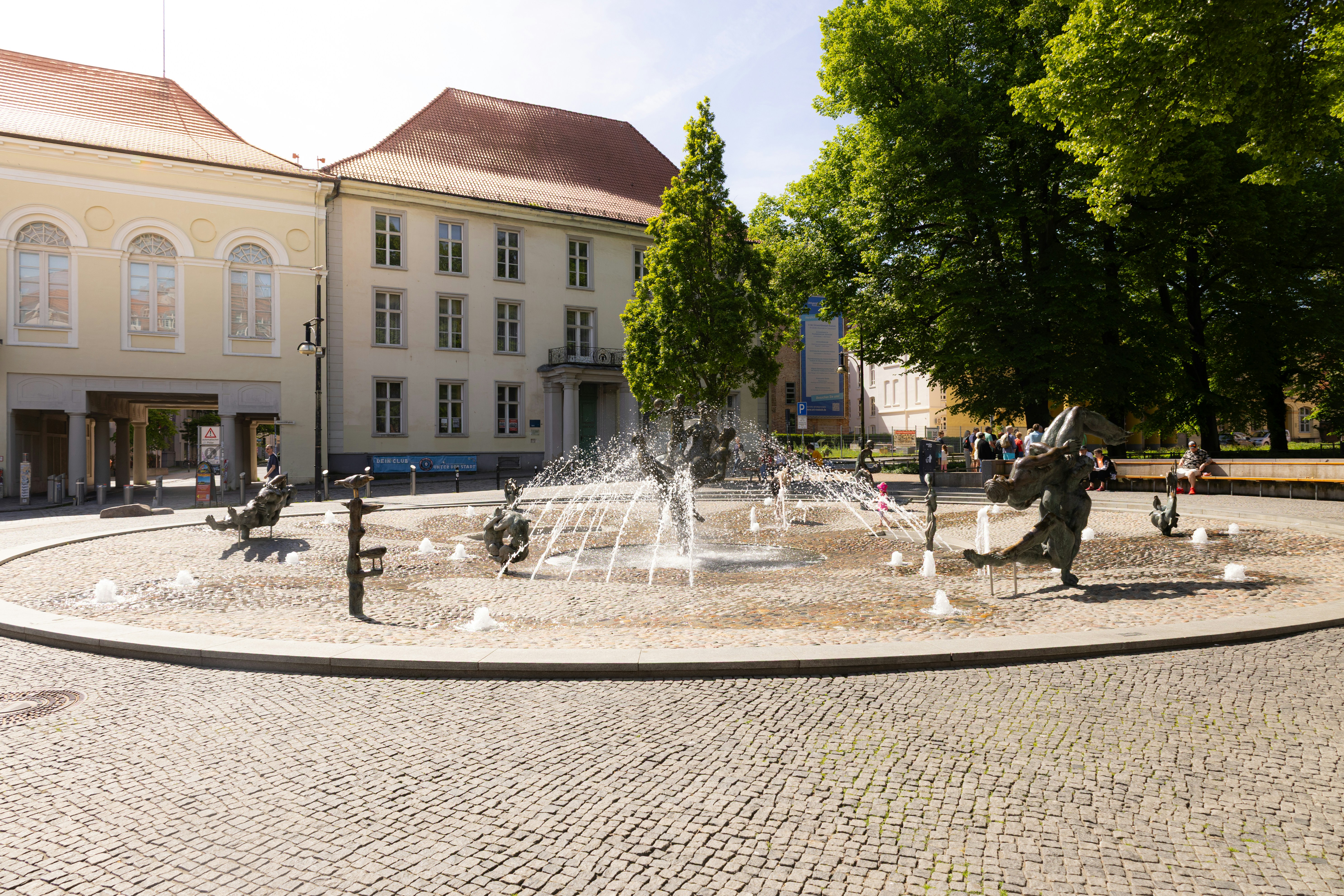 A circular fountain with sculptures in front of a building.