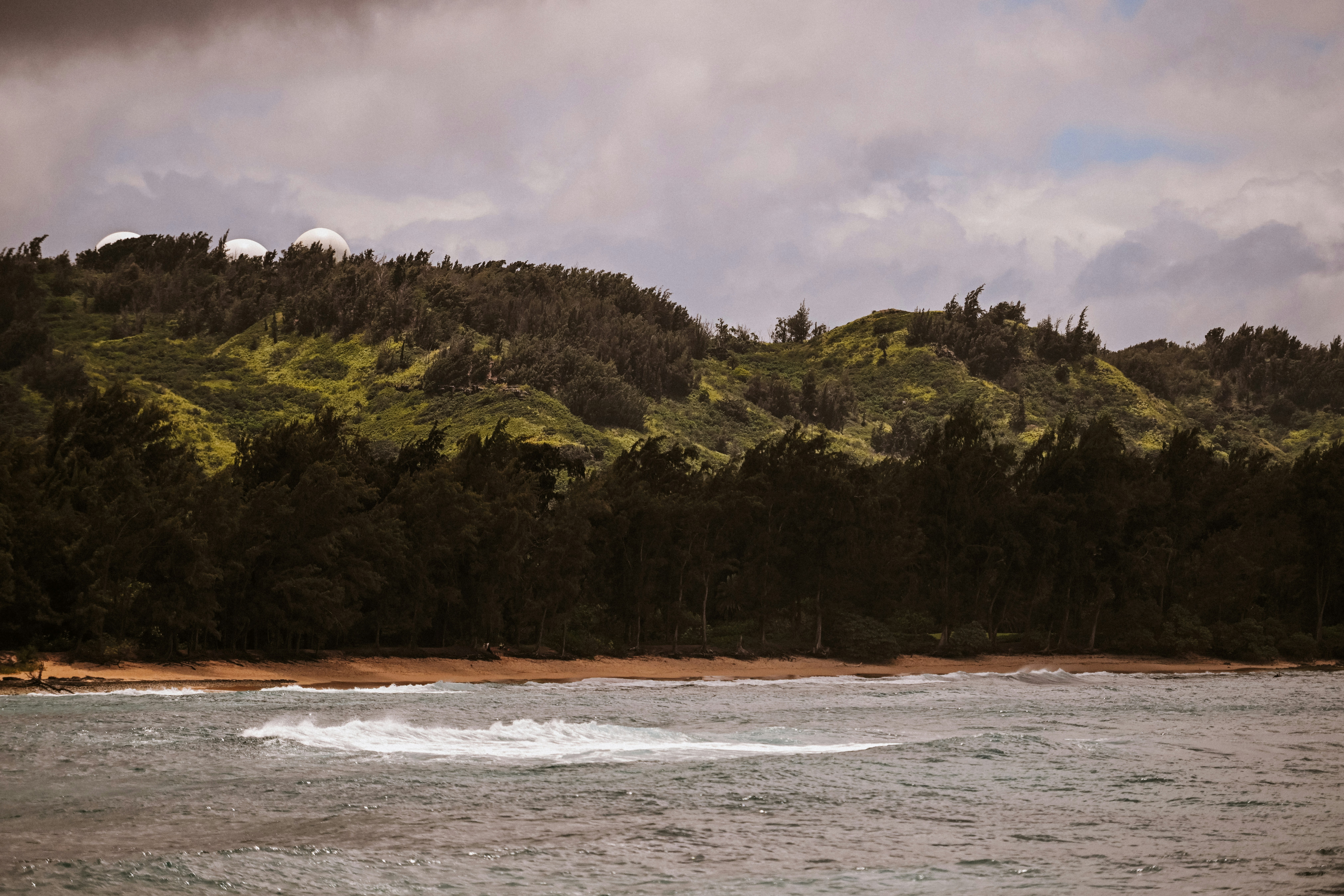 Ocean waves breaking near a sandy beach and green hills.
