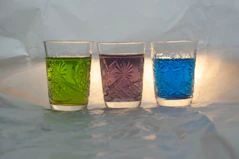 Three glasses with green, purple, and blue liquids on white.