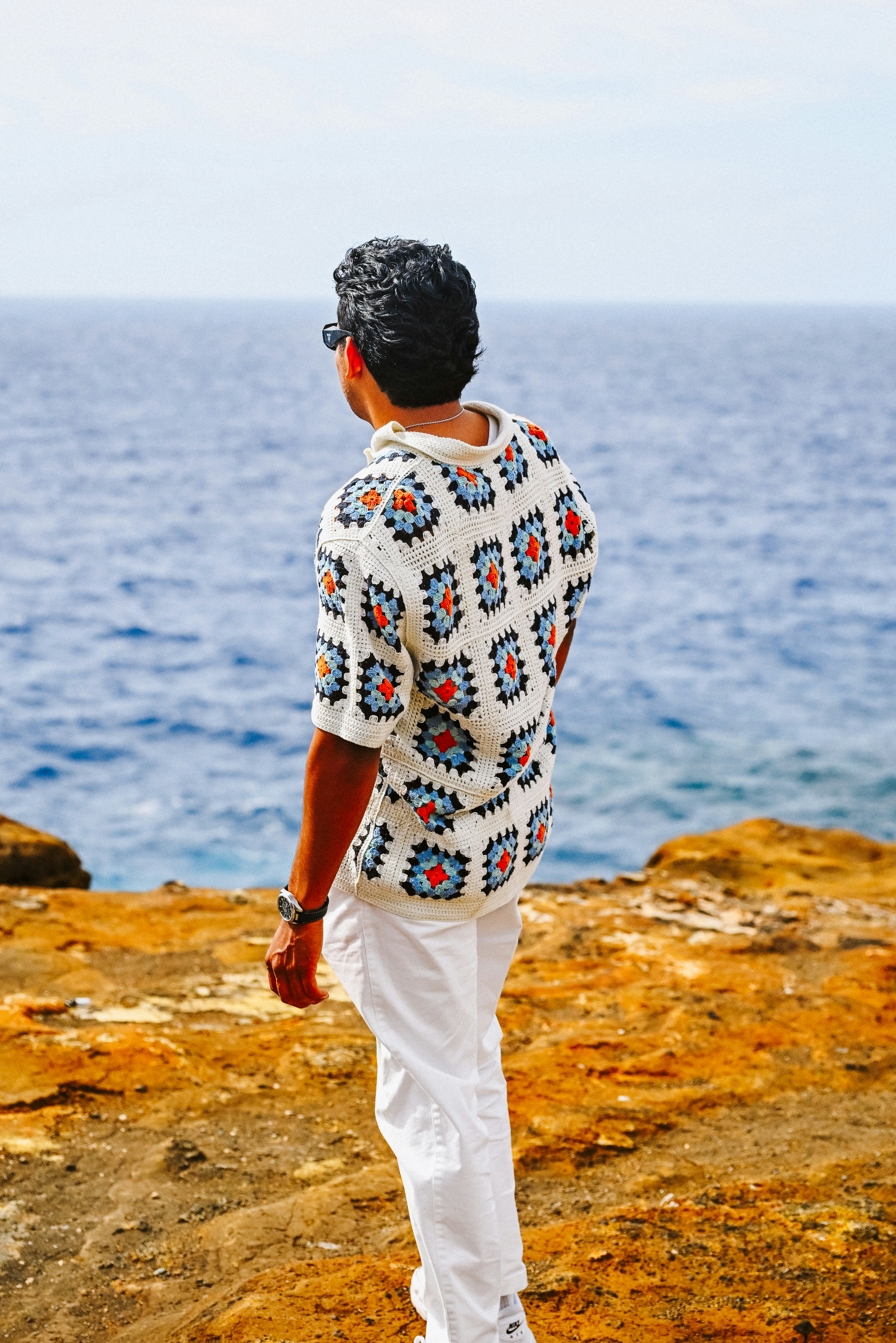Man on rocky cliff admiring the vast blue ocean.