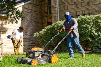 Two men mowing and trimming a residential lawn.