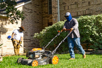Two men mowing and trimming a residential lawn.