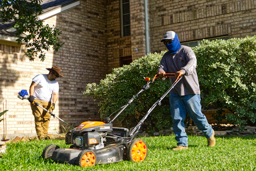 Two men mowing and trimming a residential lawn.