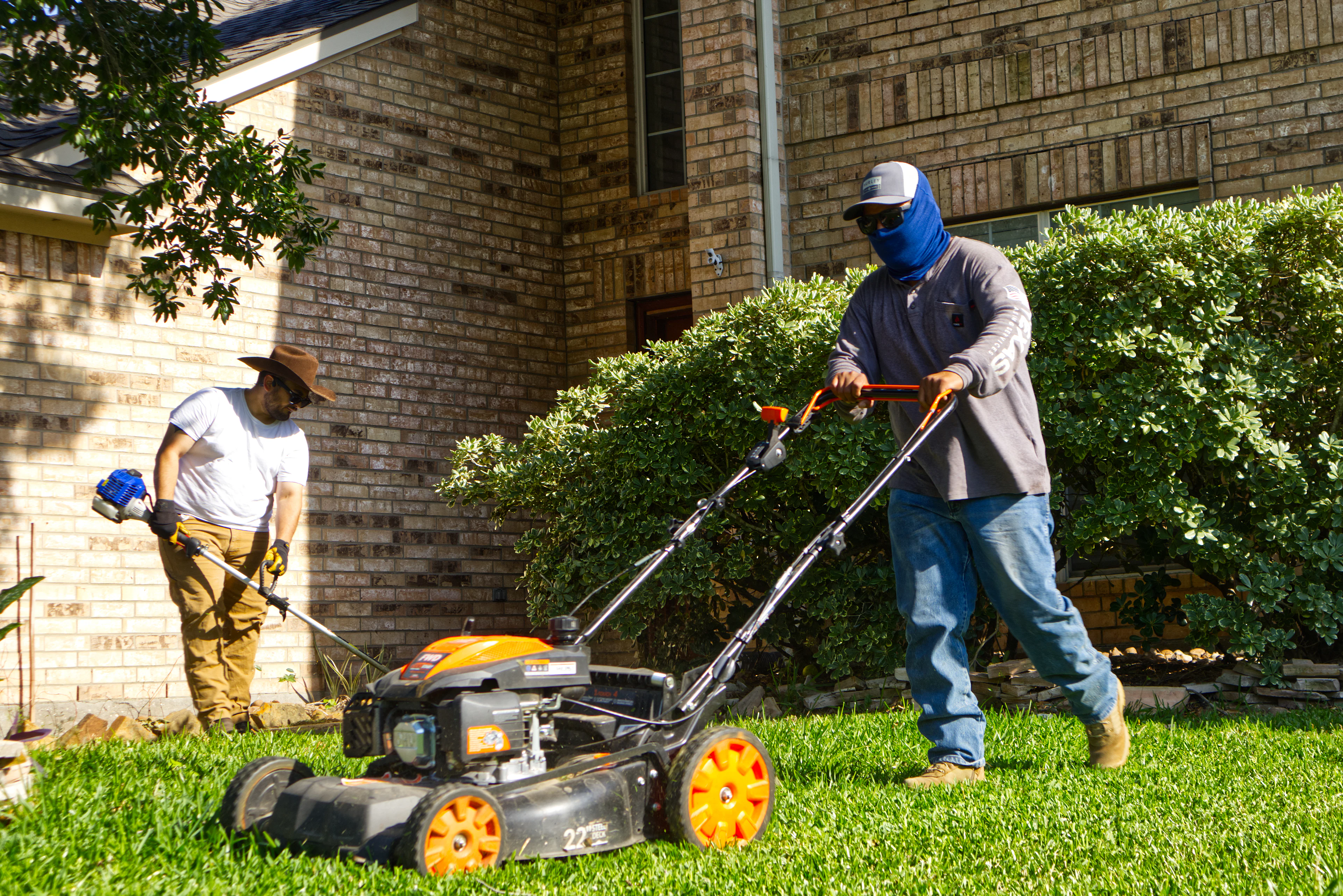 Two crew members mowing and trimming a lawn