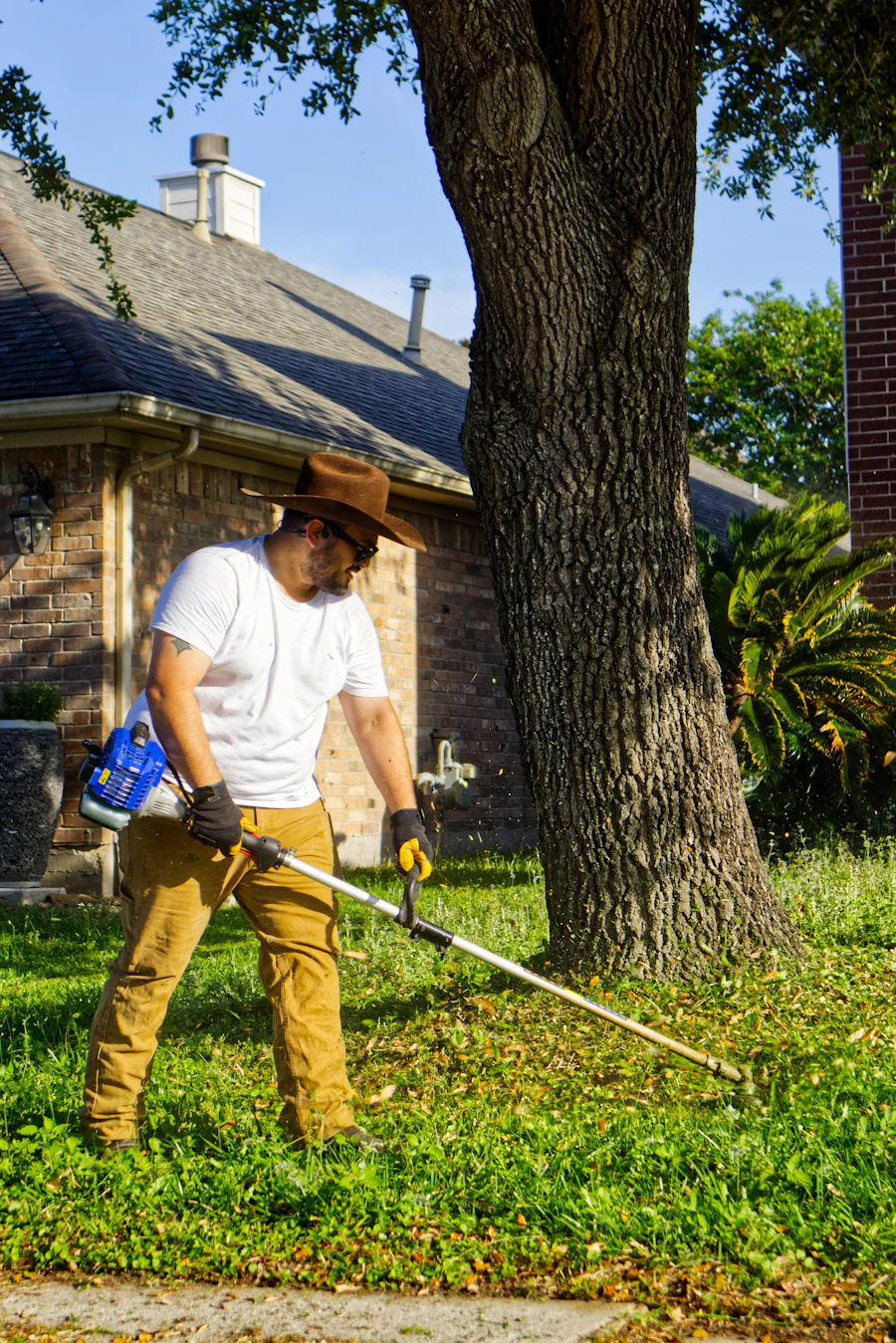 A landscaper wearing safety glasses trims a lawn edge with a string trimmer.