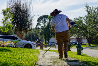 Man trimming weeds on a sunny residential sidewalk.