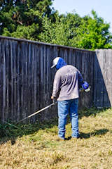 Man trims overgrown grass with a string trimmer
