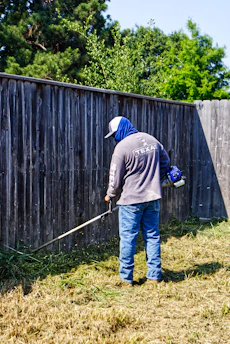 Man trims overgrown grass with a string trimmer