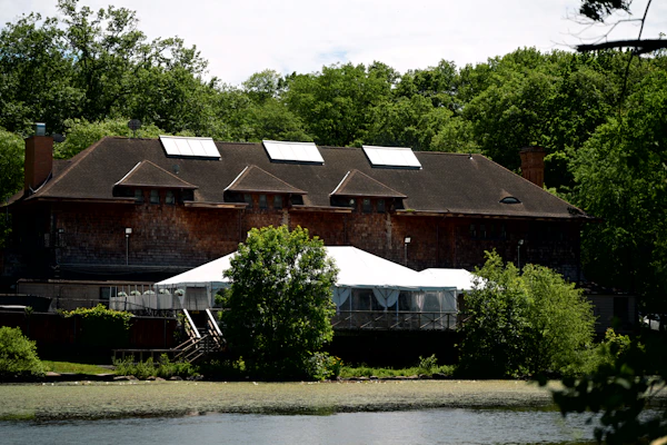 A wooden lodge on a shore with a white reception tent on the lawn beside the water