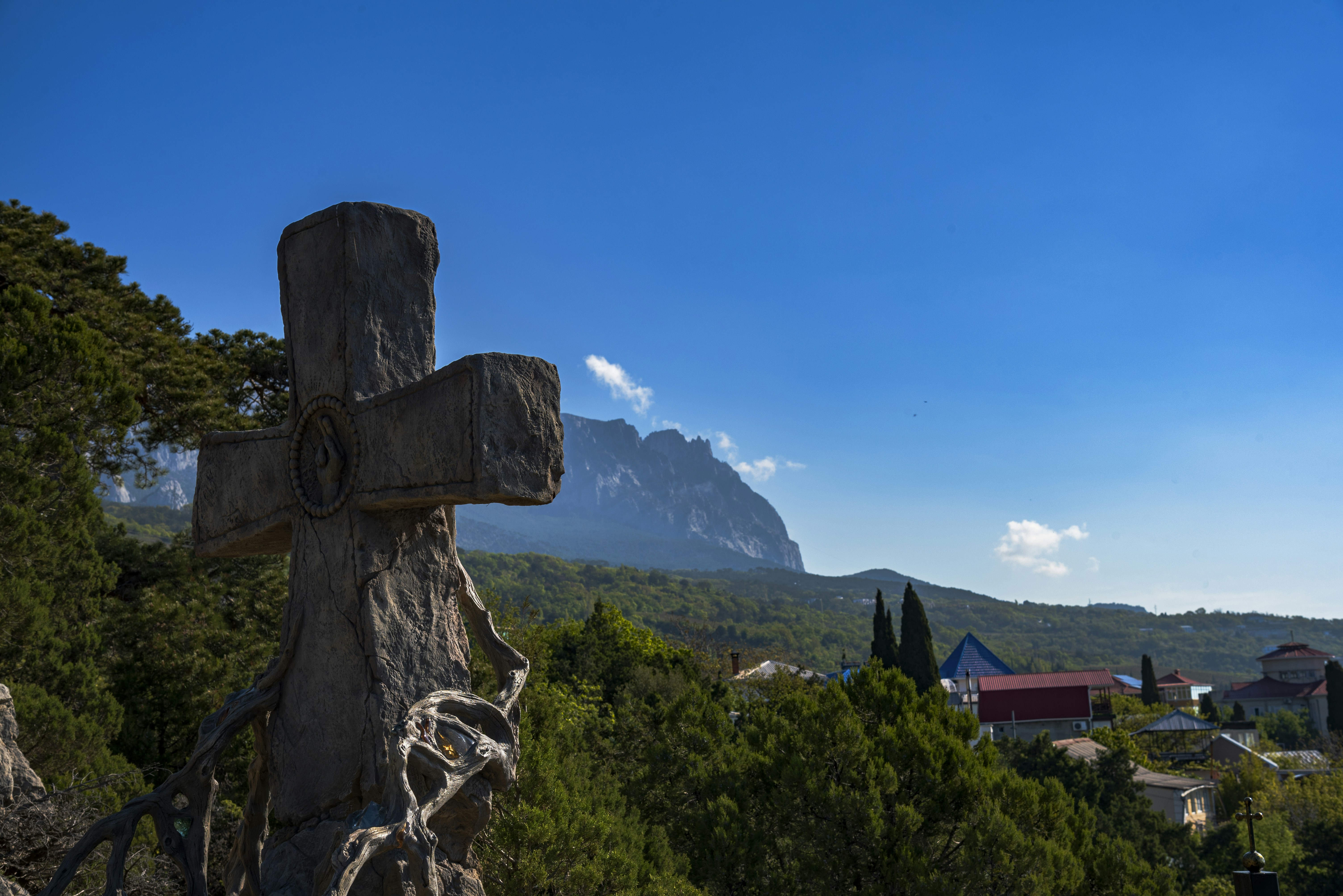 Stone cross in foreground with mountain and village background.