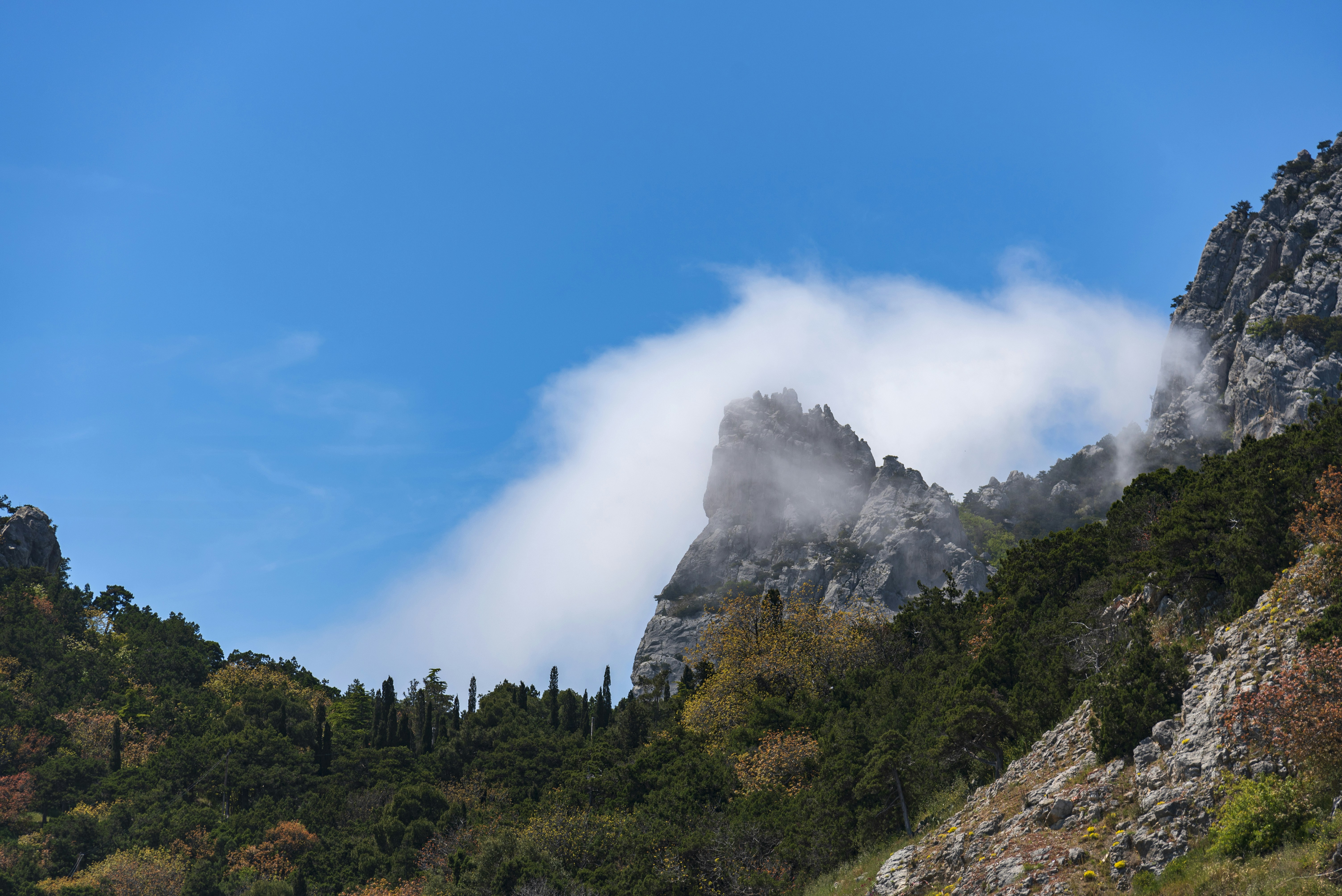 Clouds partially obscure rugged mountain peaks under a blue sky.