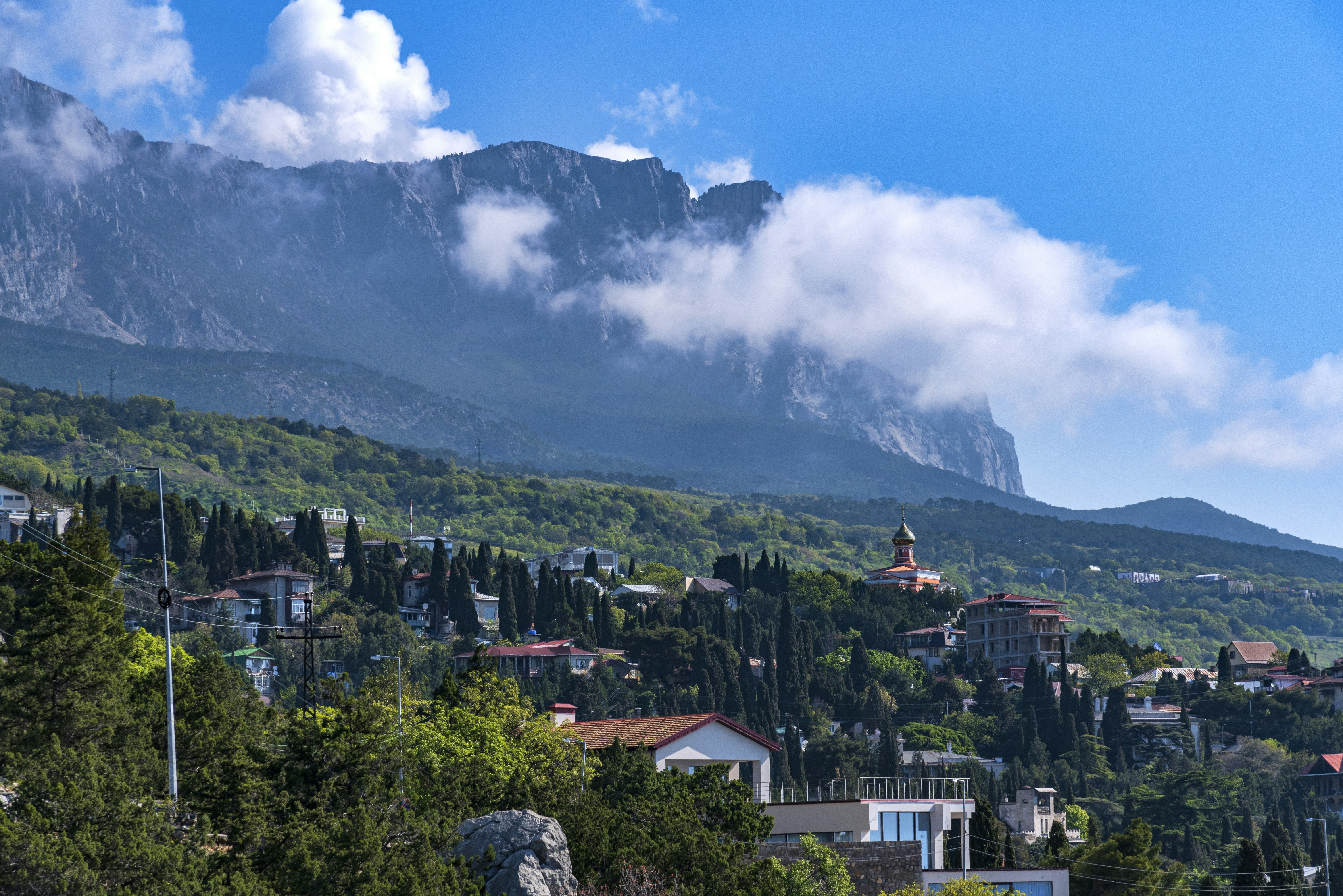 Village on a green hillside beneath a cloudy mountain.