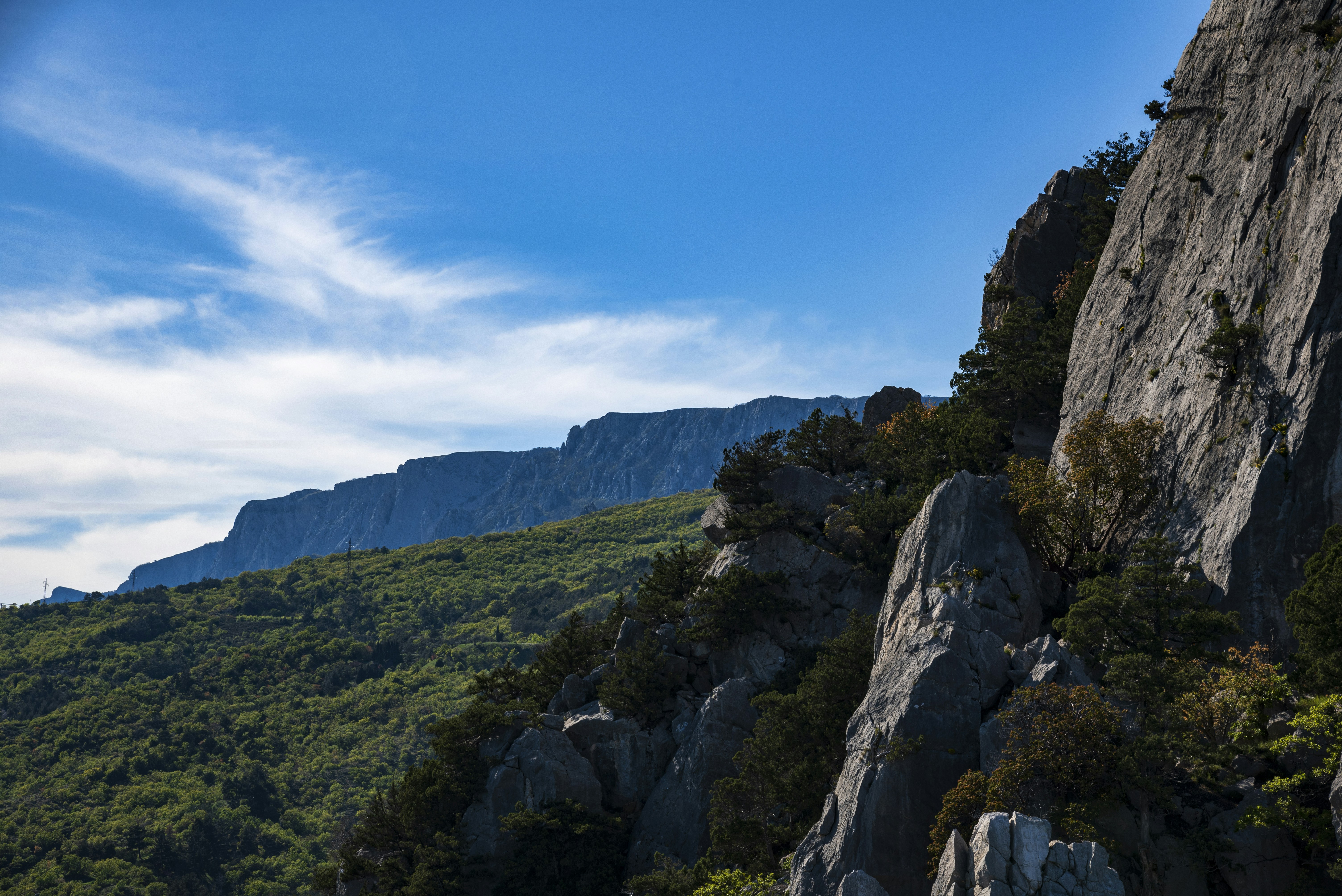 Green mountains and rocky cliffs under a clear blue sky.