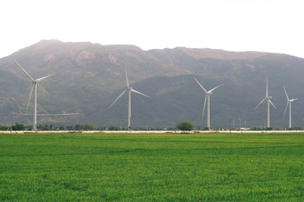 Five wind turbines stand in a green field before mountains