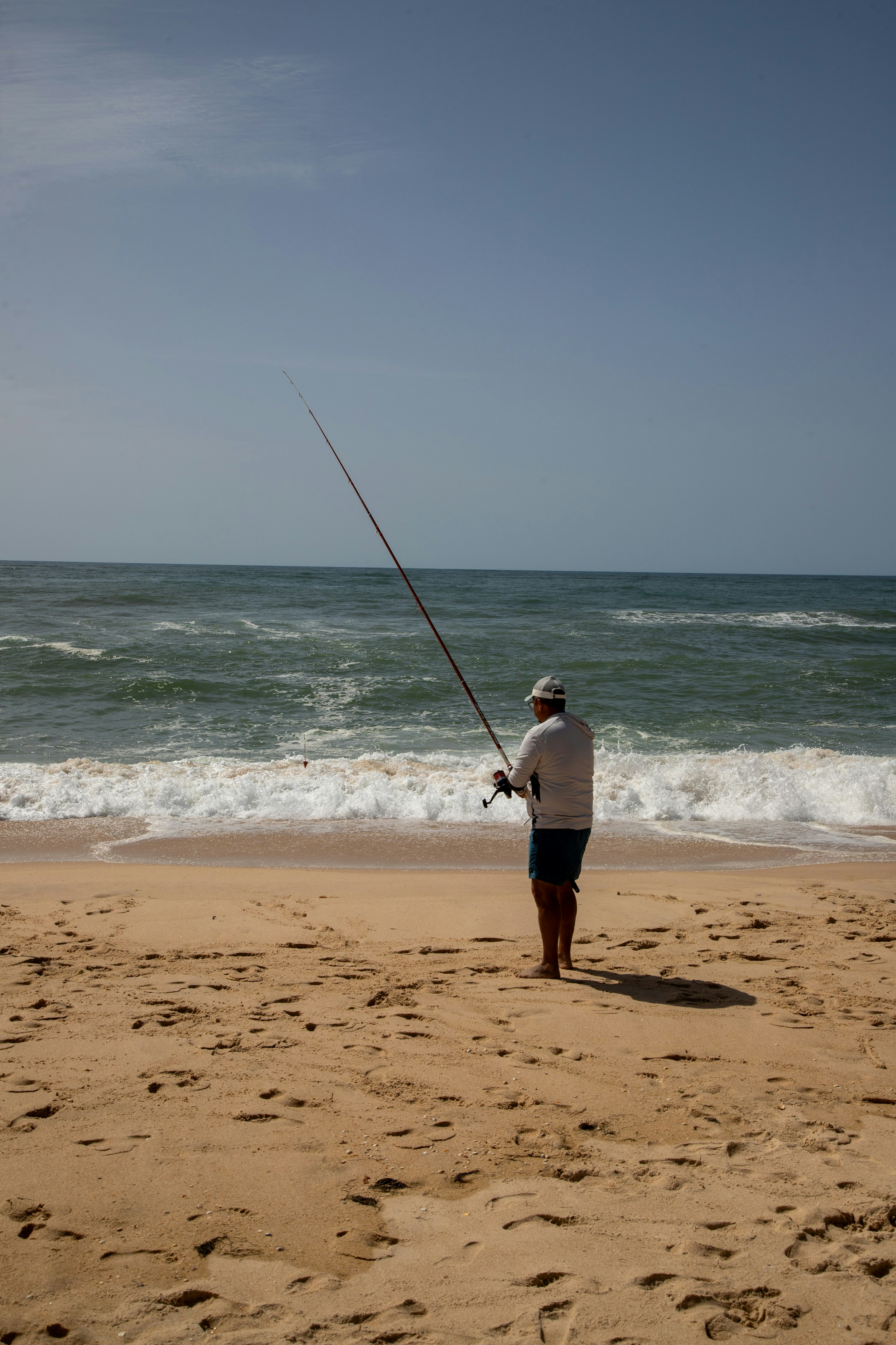 Ein Mann, der an einem Sandstrand am Meer angelt.