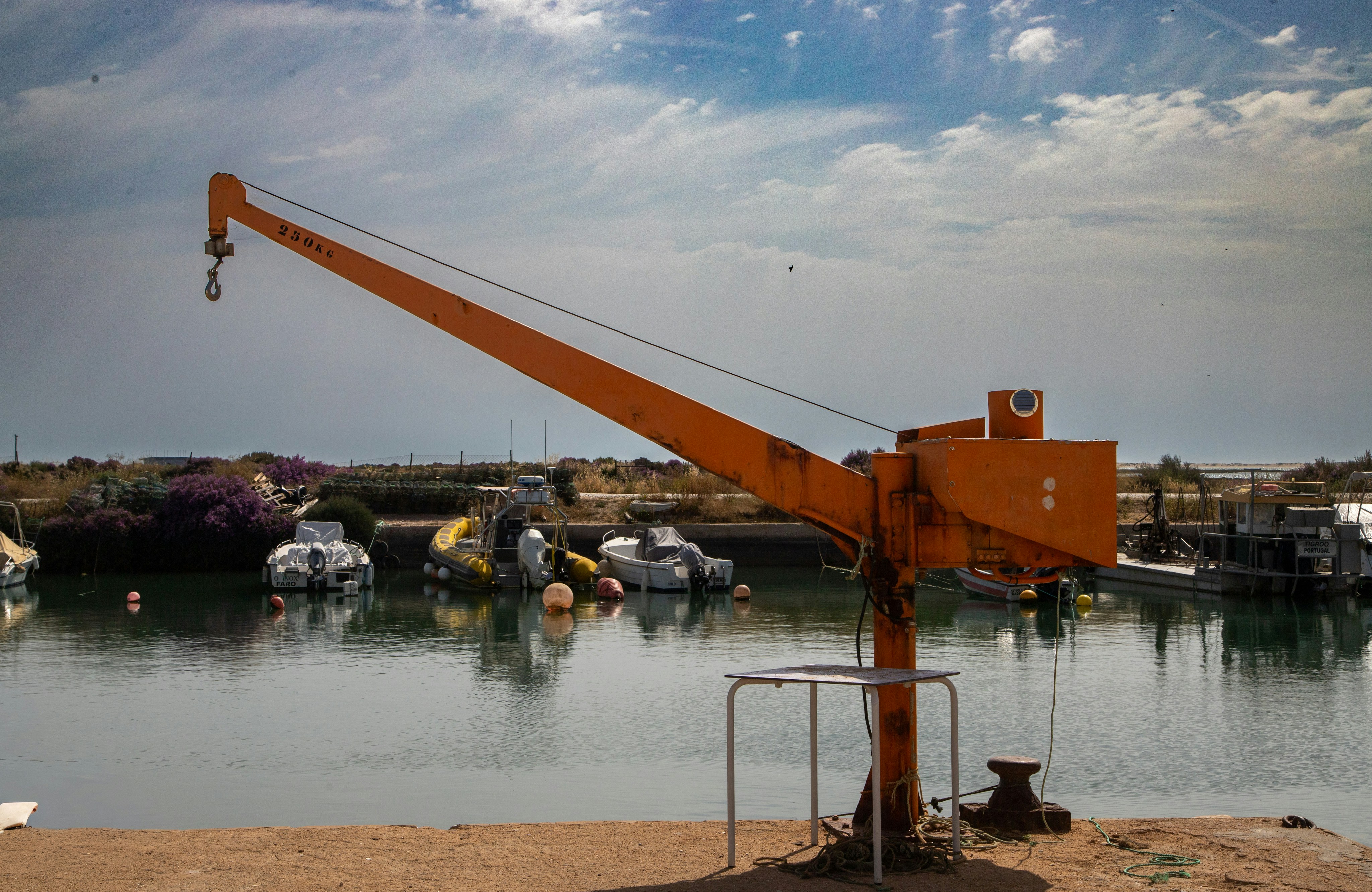 Orange crane on a dock with boats in a harbor.
