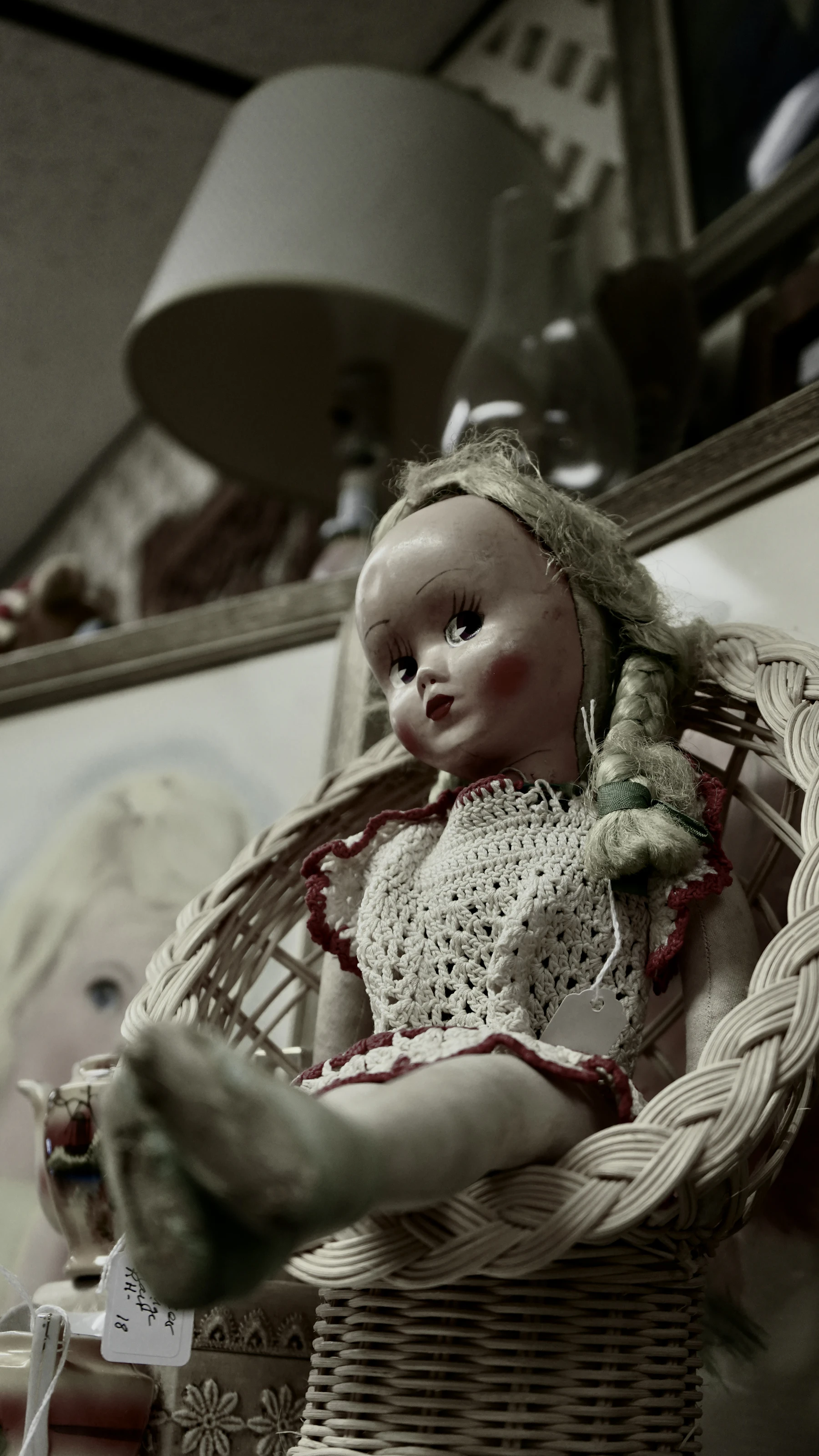 A braided vintage doll with paper price tags sitting in a wicker chair in a shop