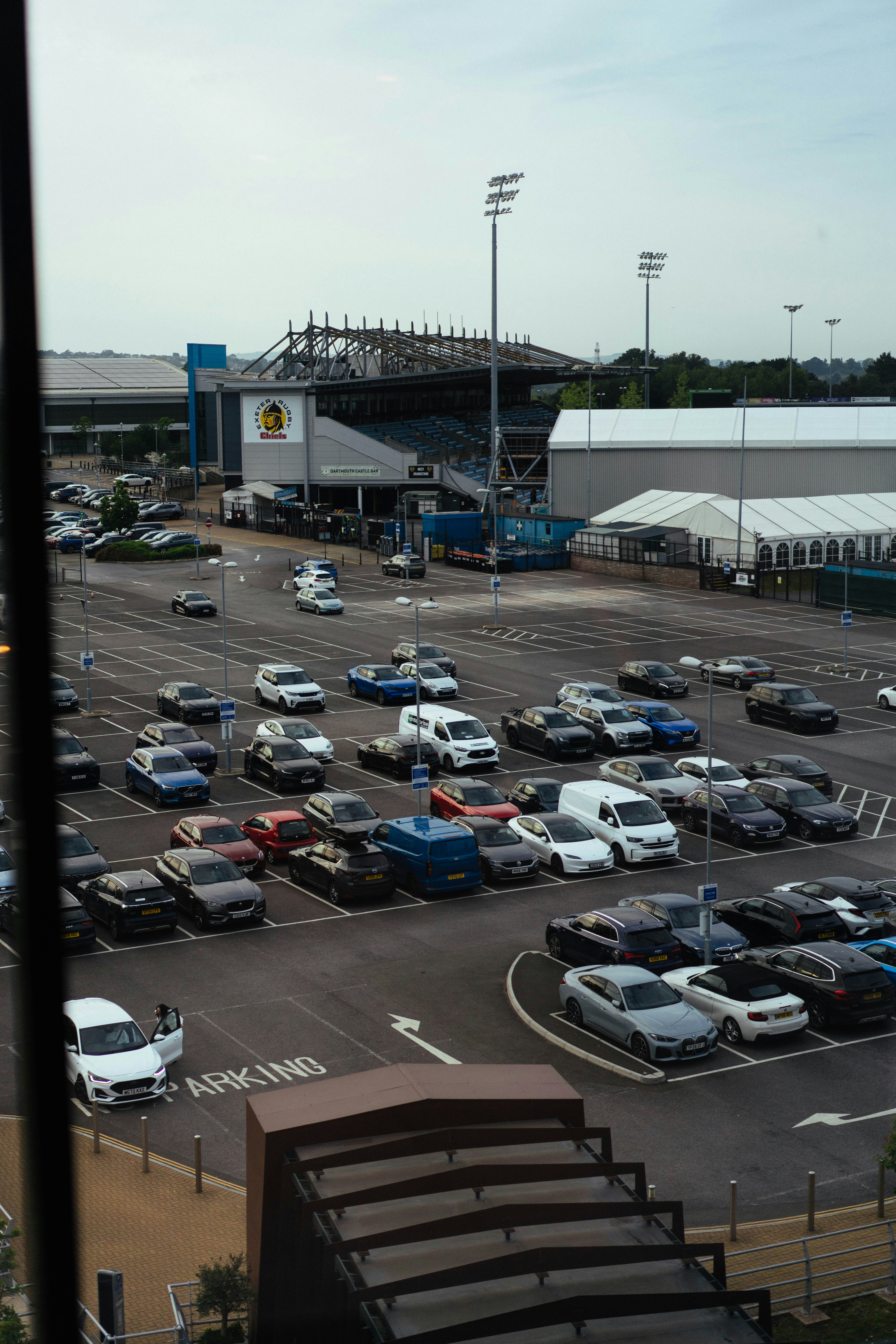 Des voitures garées sur un grand parking à côté d’un stade.