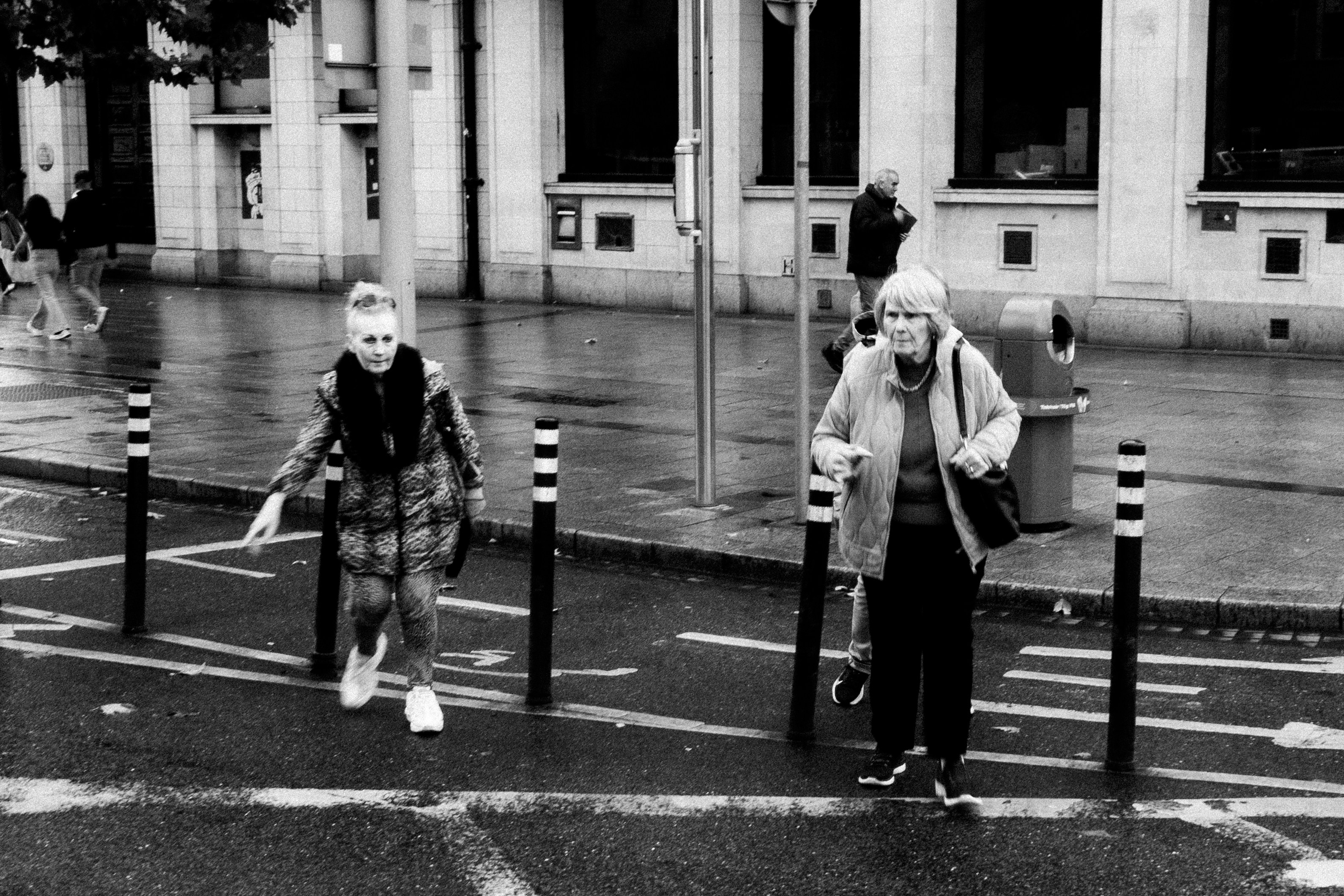 Two pedestrians crossing a wet urban street.