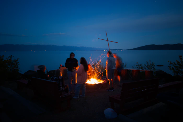 Group gathered around a bonfire beside water