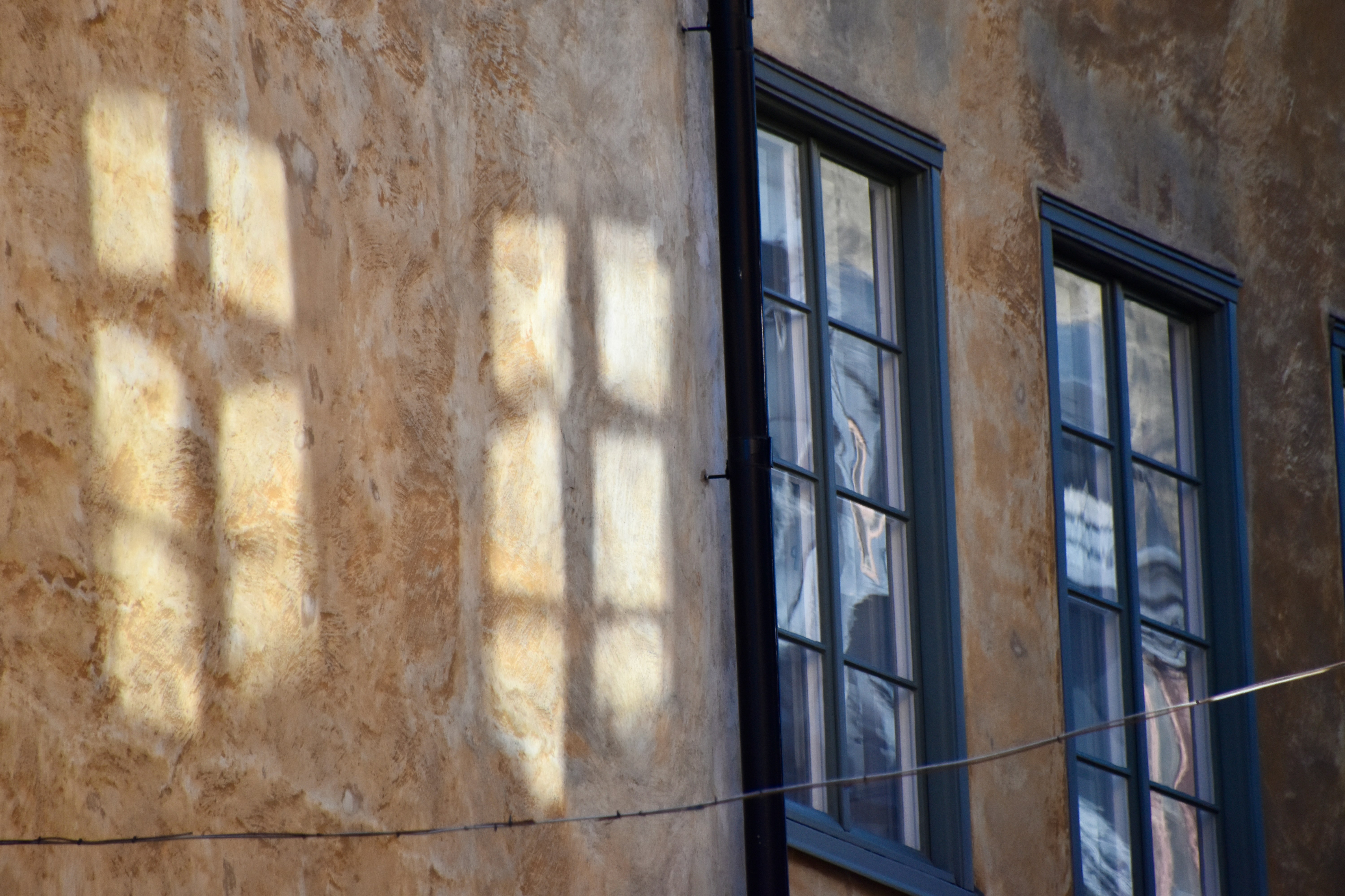 Sonnenlicht wirft Fensterschatten auf eine alte Gebäudewand.