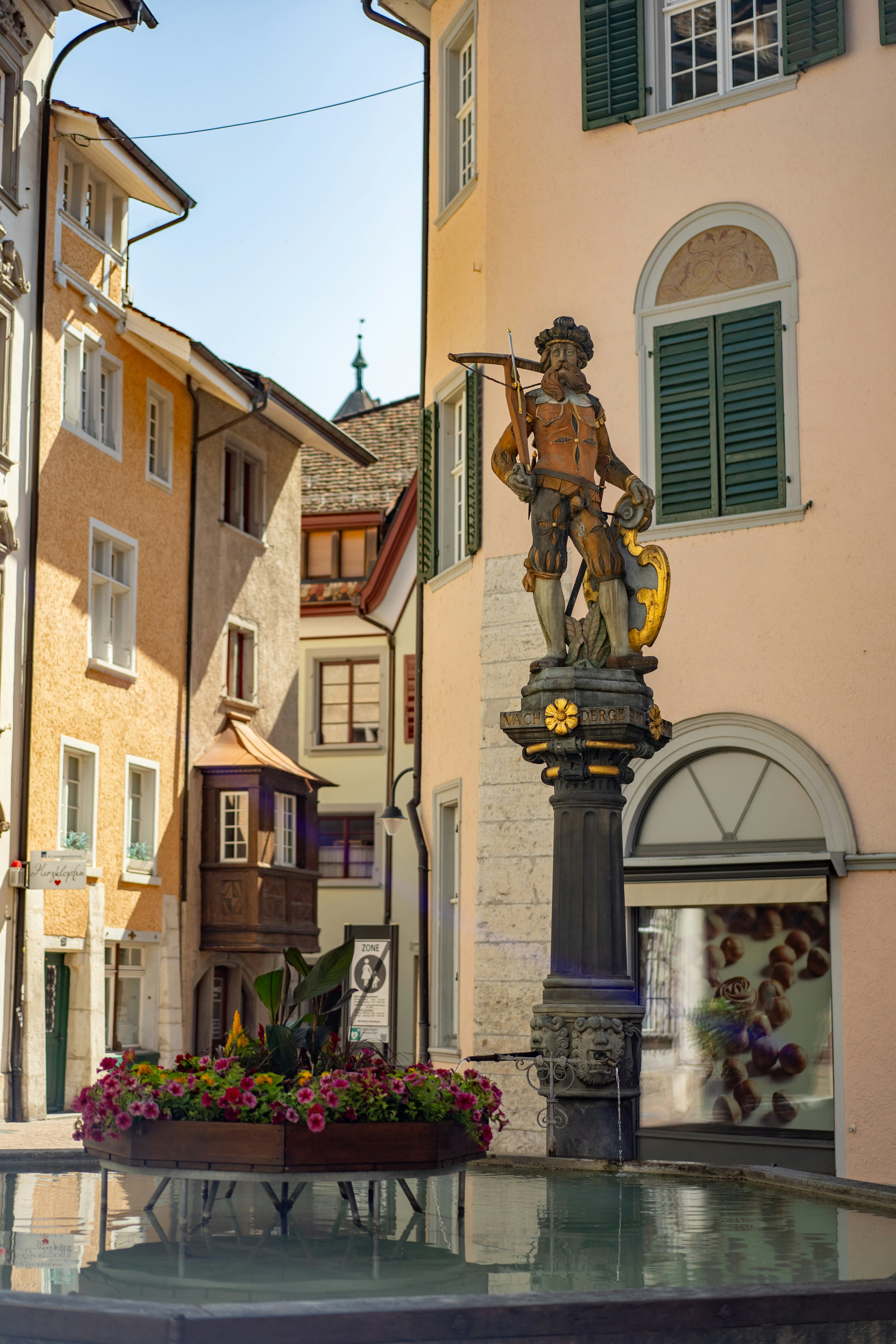 Fontaine historique avec une statue au milieu de vieux bâtiments européens.