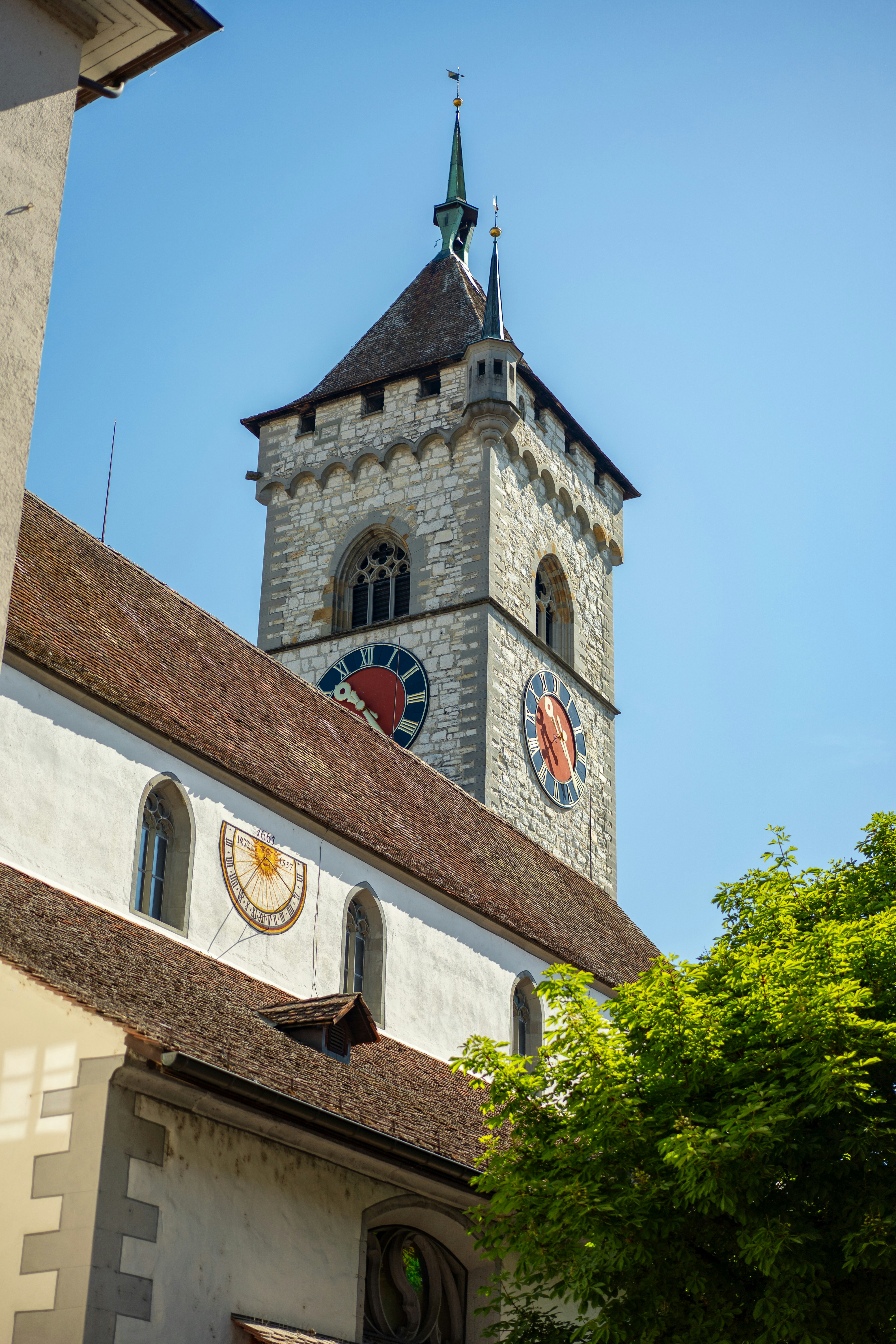 Tour d’horloge en pierre et bâtiment avec cadran solaire sous un ciel dégagé.