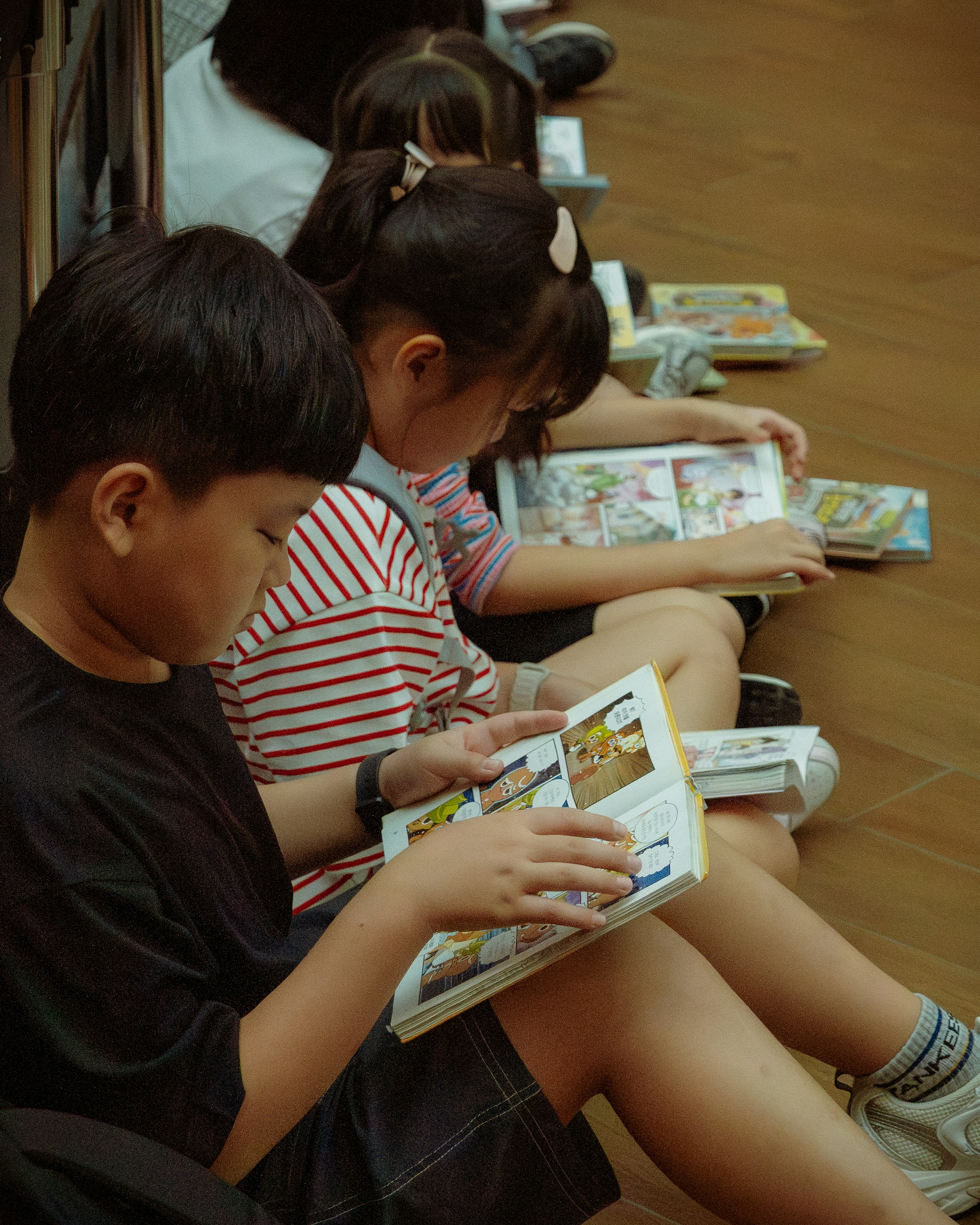 Young children quietly read comic books on the floor.