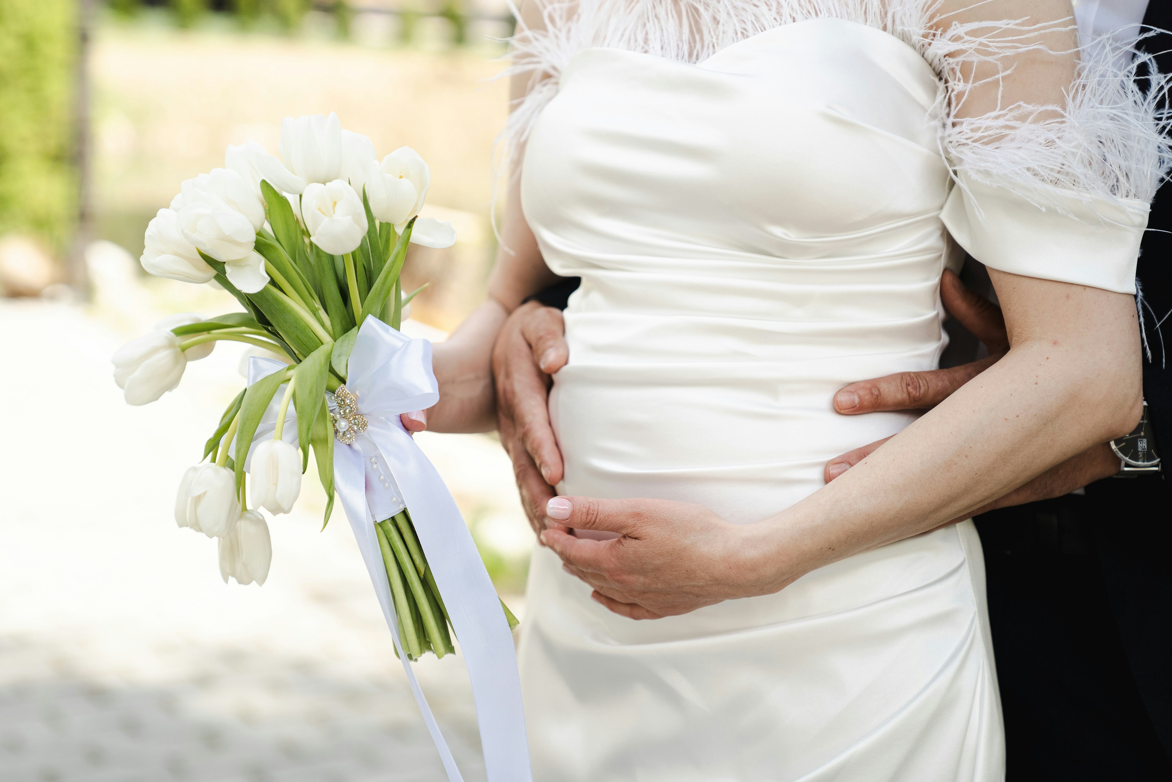 Weißes Hochzeitskleid, Tulpenstrauß und umarmende Hände.