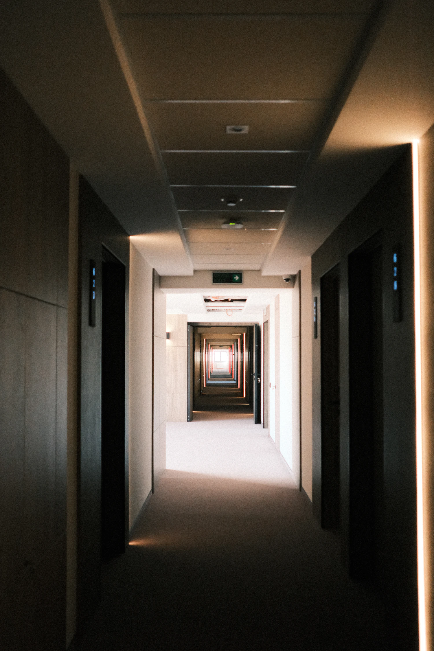 A dim corridor with doors receding into one pool of warm light
