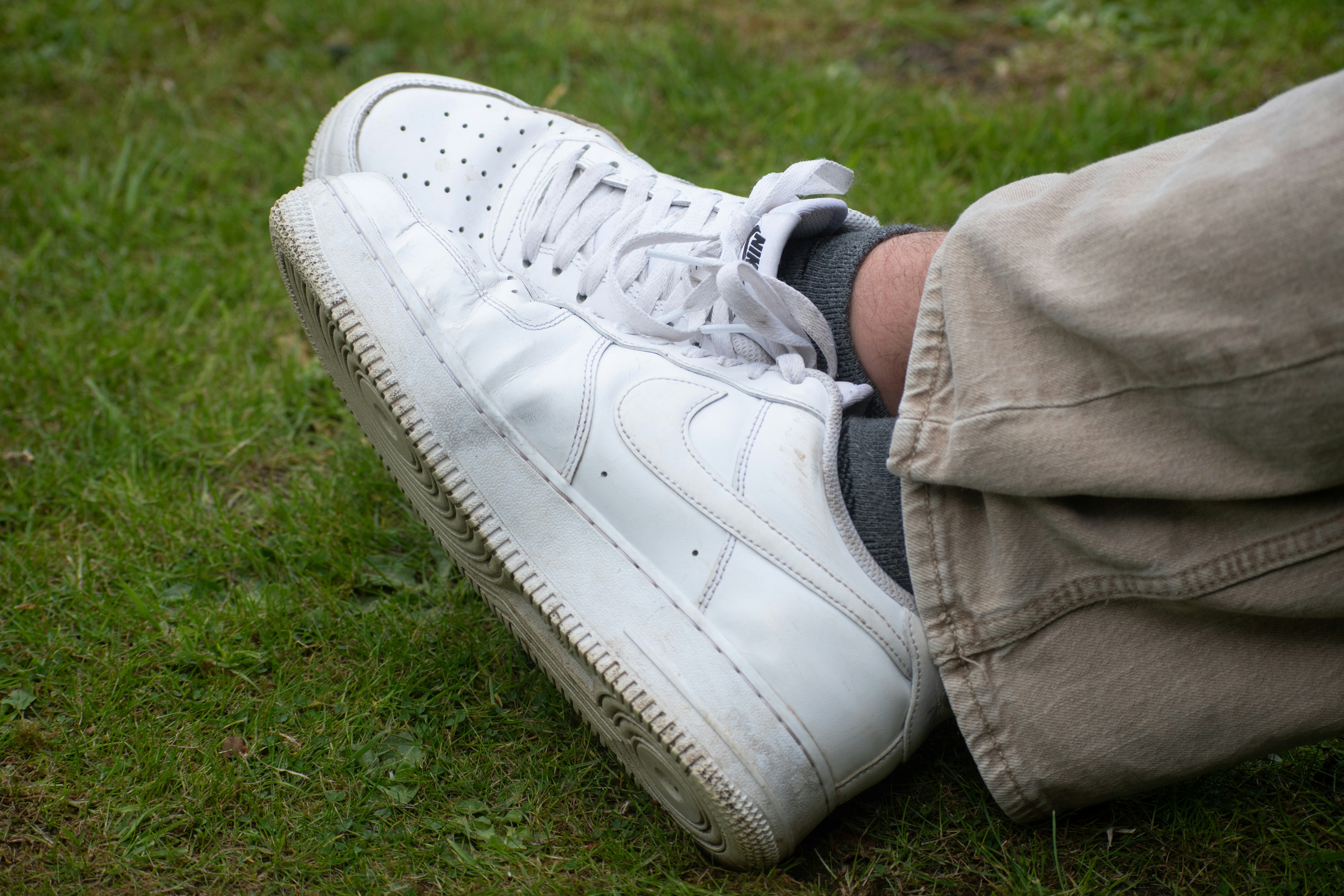 White sneakers and khaki pants resting on green grass.