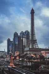 Eiffel tower replica and modern buildings under a cloudy sky.