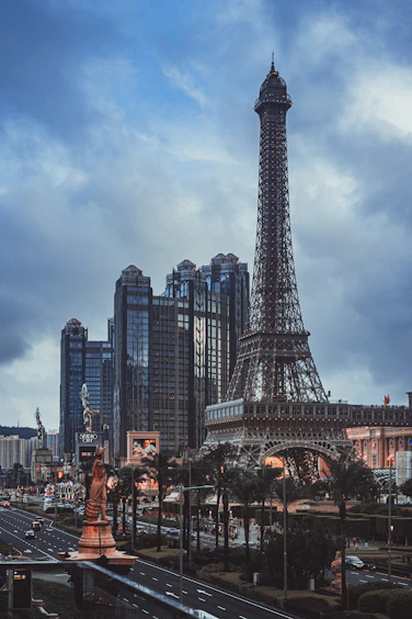 Eiffel tower replica and modern buildings under a cloudy sky.