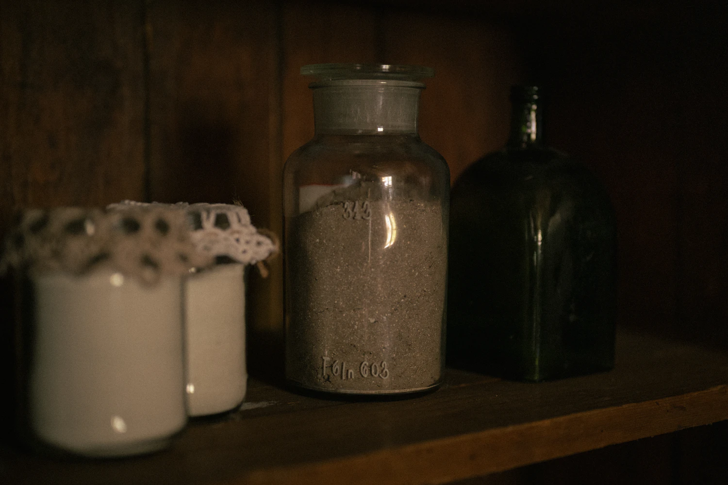 A row of old glass jars and bottles standing on a dark wooden shelf