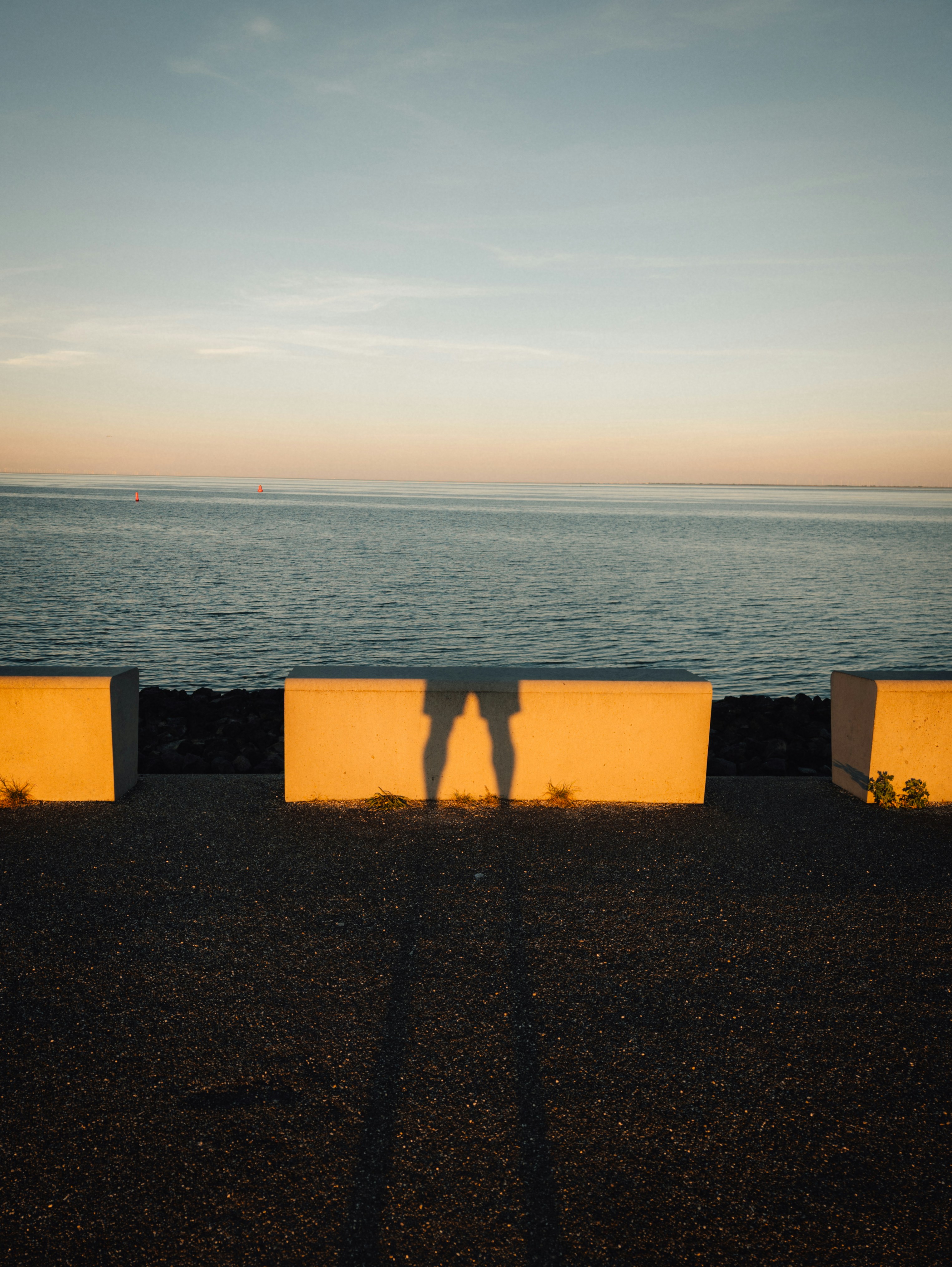 Shadow of legs on golden barrier by calm sea.