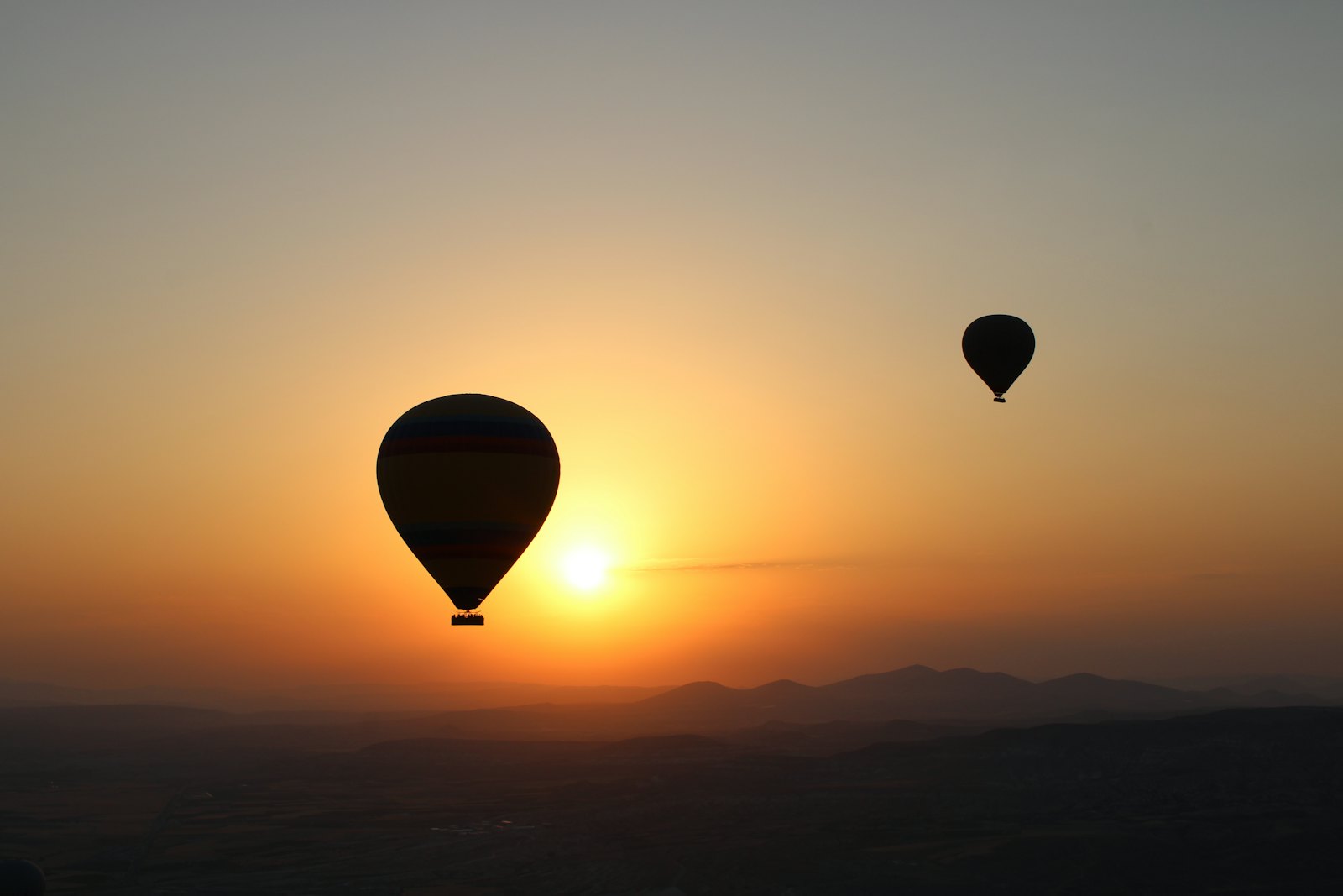 Two hot air balloons drifting over open terrain at first light