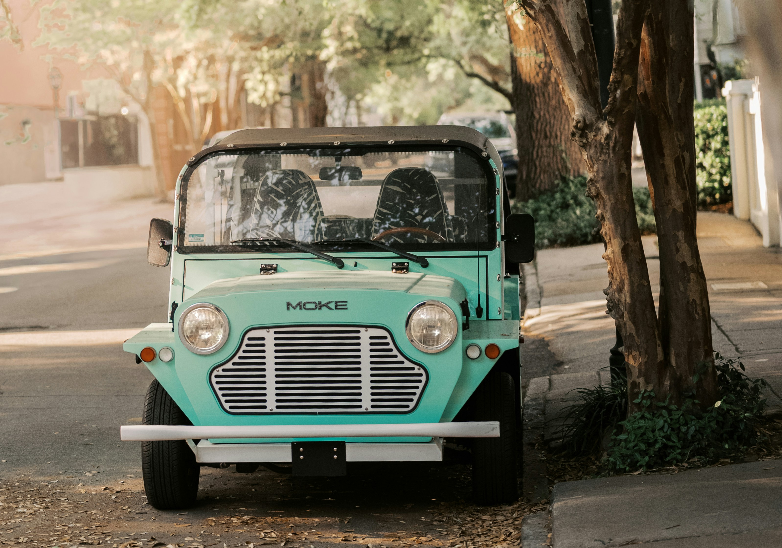 Sebuah mobil moke biru muda diparkir di jalan yang cerah.