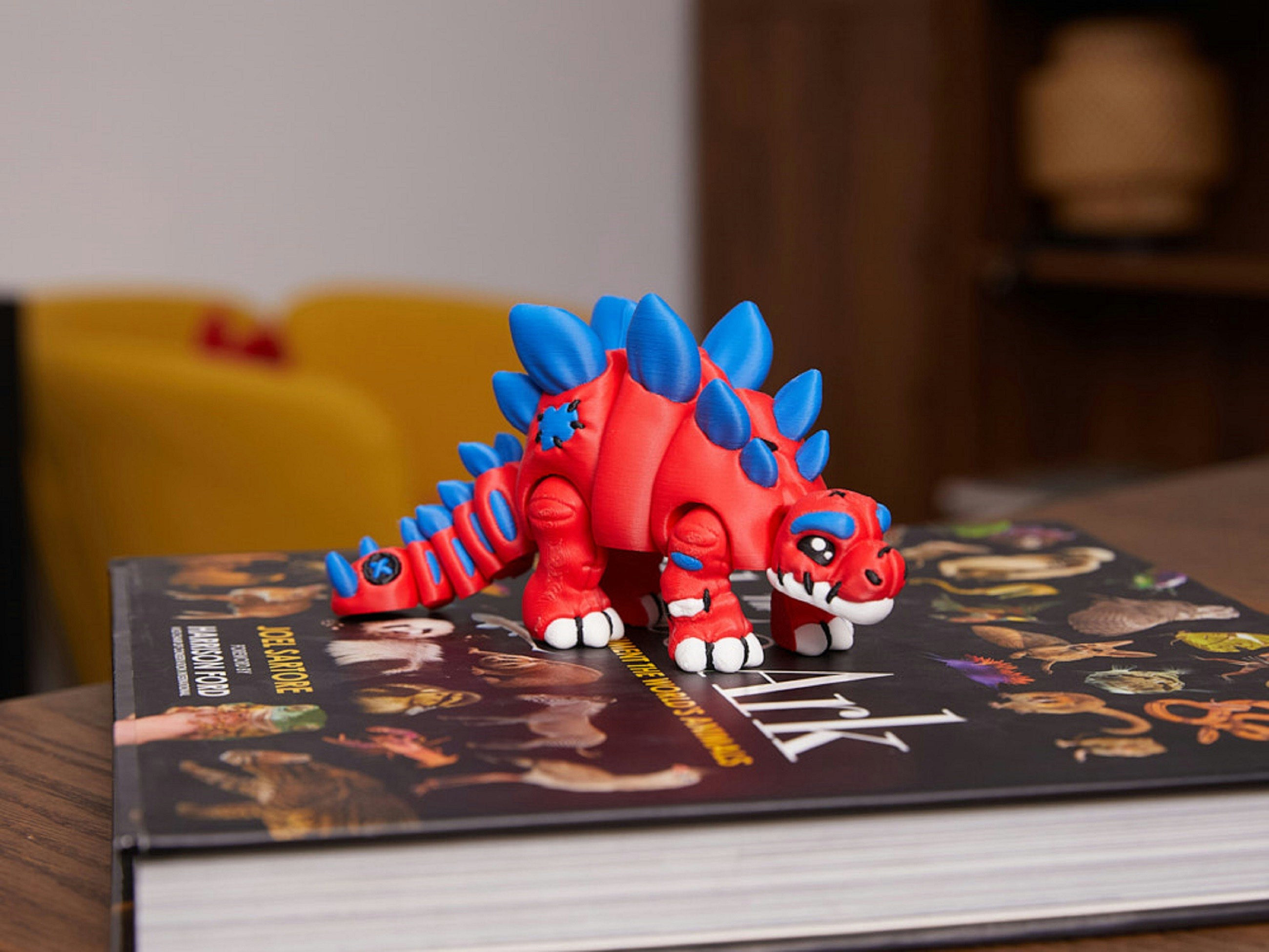 Ein rot-blauer Spielzeugdinosaurier sitzt auf einem Buch.