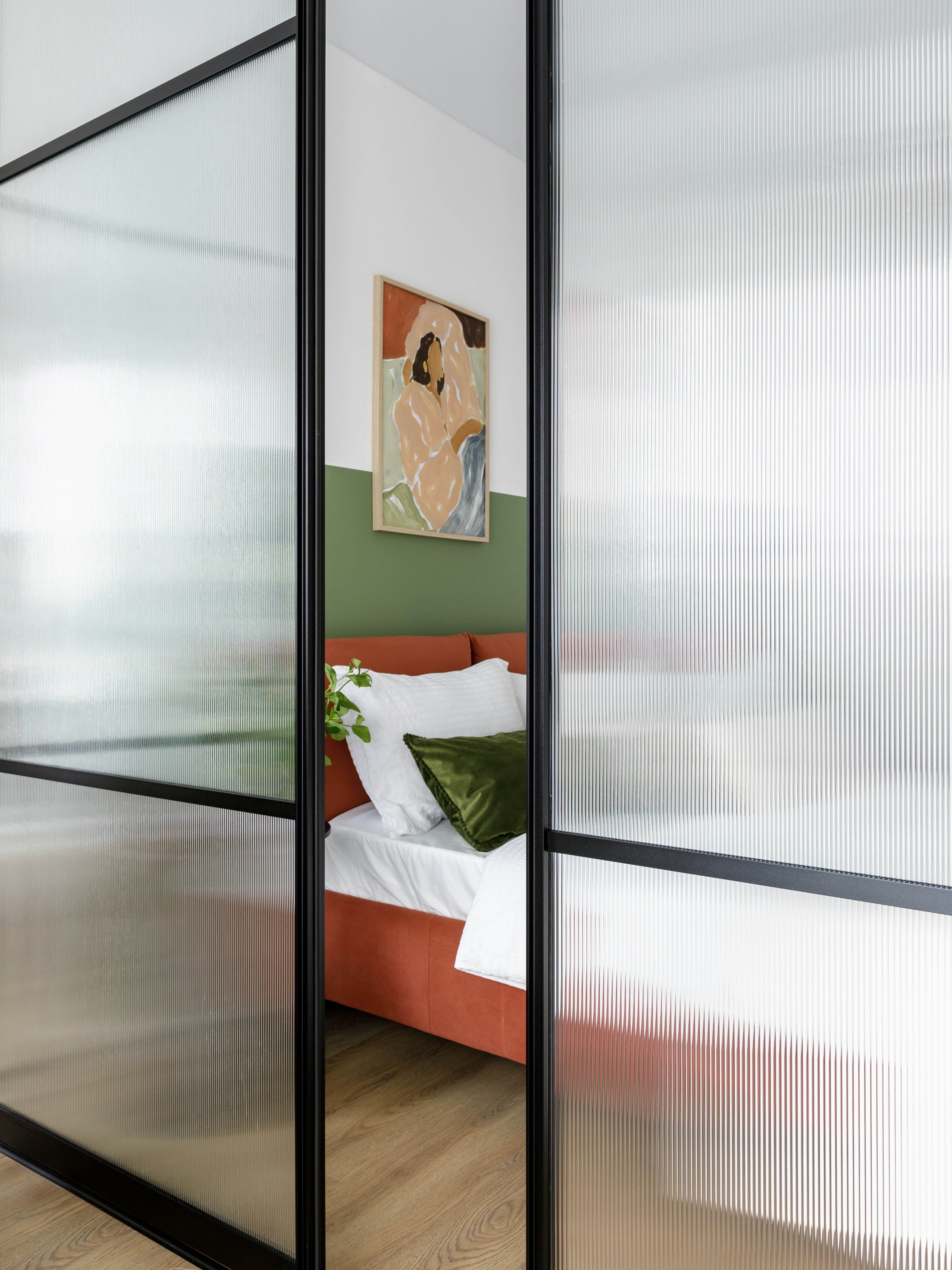 Orange bed, green pillows, and art behind frosted glass partition.