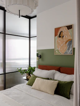 Modern bedroom with orange headboard, painting, and frosted glass partition.