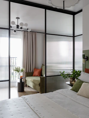 Modern bedroom separated by frosted glass partition and green sofa.