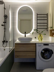 Modern bathroom with backlit mirror, washing machine, and bathtub