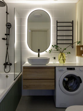 Modern bathroom with backlit mirror, washing machine, and bathtub