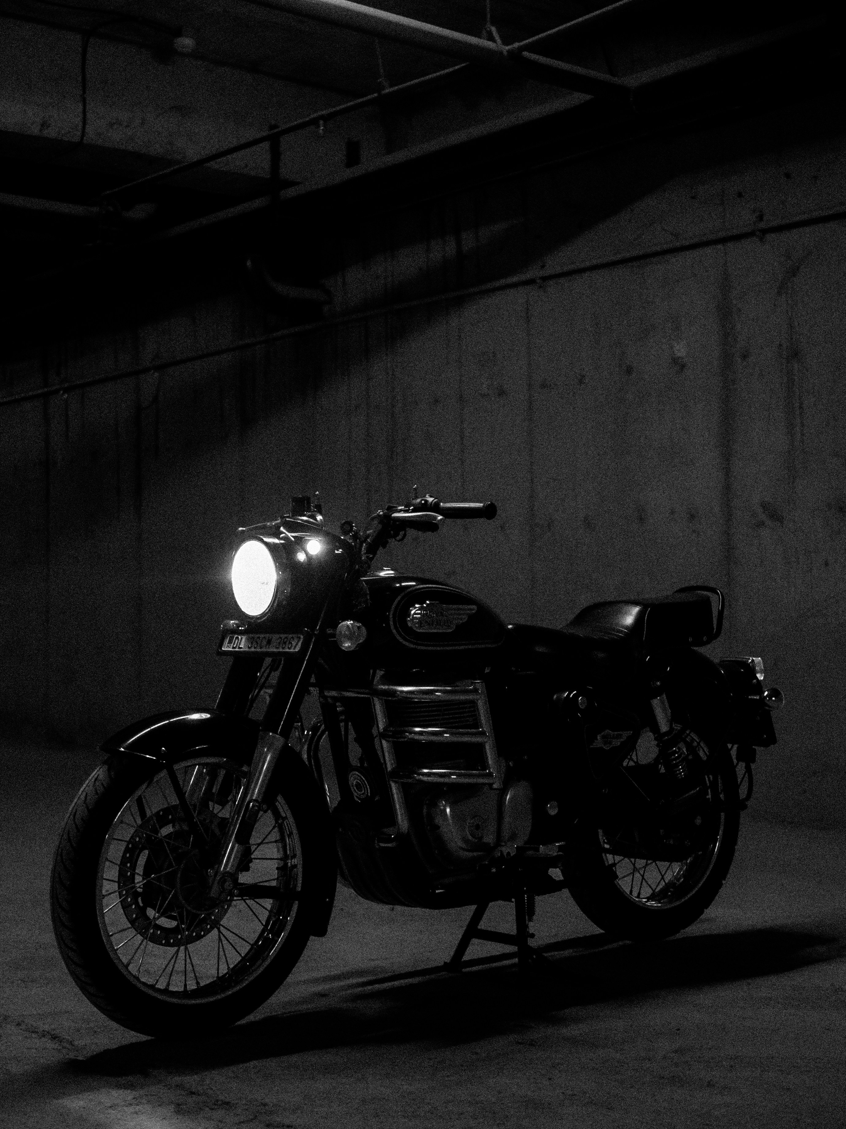 Classic motorcycle with bright headlight on in dark garage.