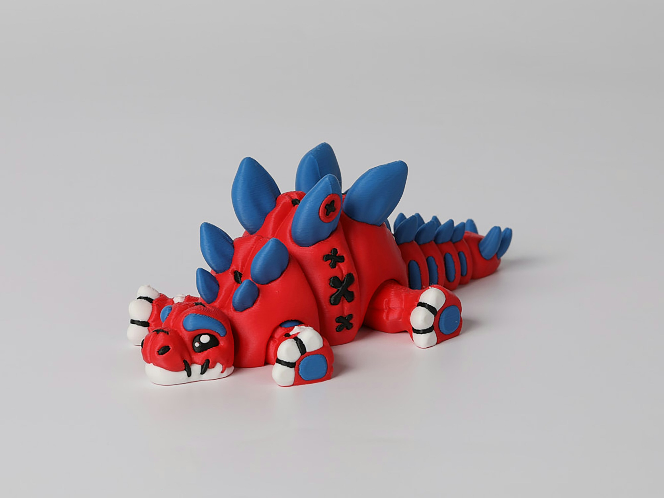 Rotes und blaues Ton-Stegosaurus-Spielzeug auf einer weißen Oberfläche.
