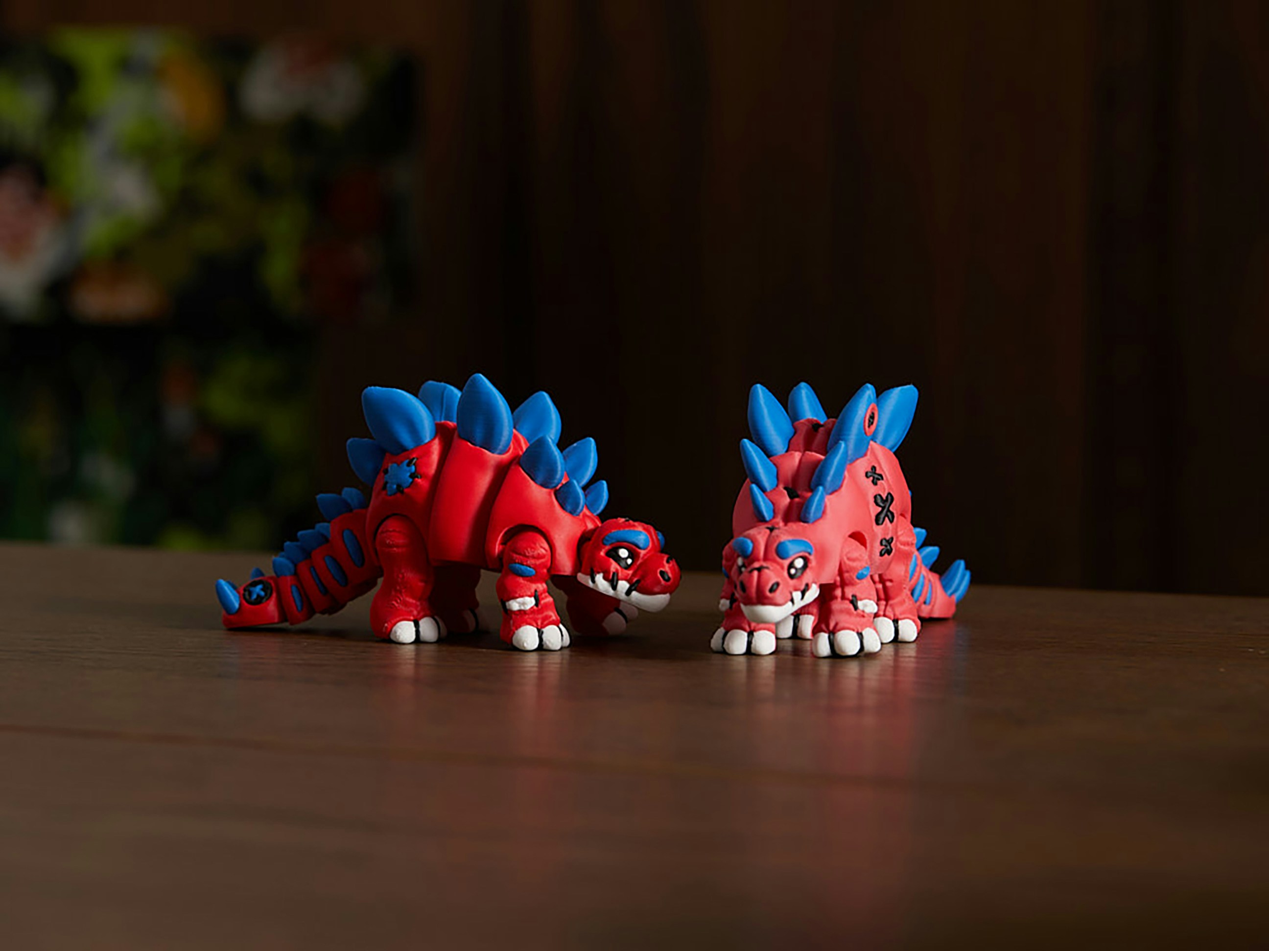 Zwei rote und blaue Dinosaurierspielzeuge auf einem Holztisch.